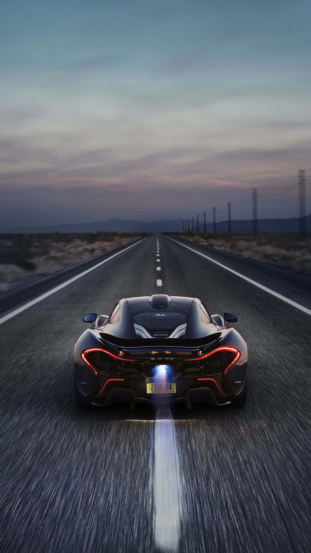 汽車 桌布 壁紙 — 一輛黑色McLaren P1在黃昏時分疾馳在沙漠公路上，尾燈閃爍，帶有動態模糊效果。