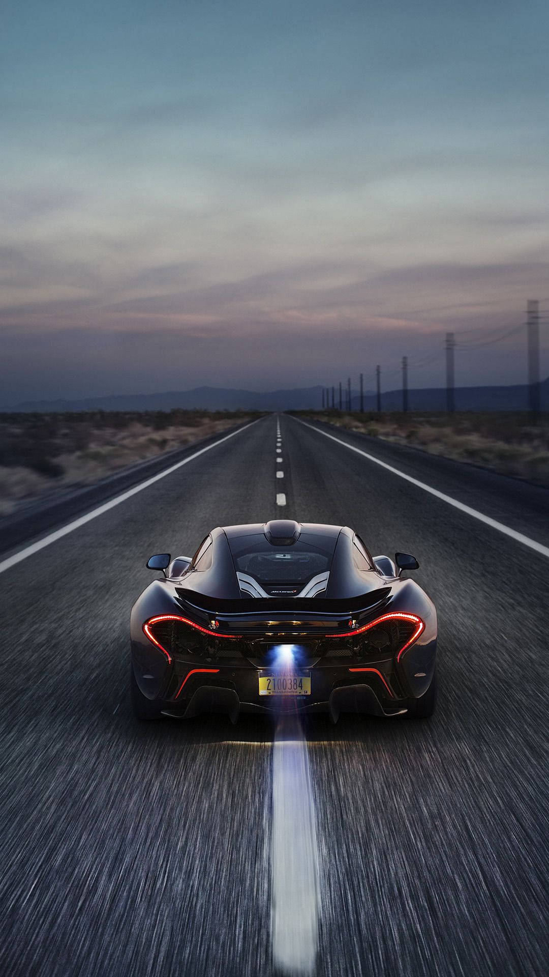 紅色動圖 桌布 壁紙 — 一輛黑色McLaren P1在黃昏時分沿沙漠高速公路飛馳，紅色尾燈閃爍，排氣管噴出明亮氣流。