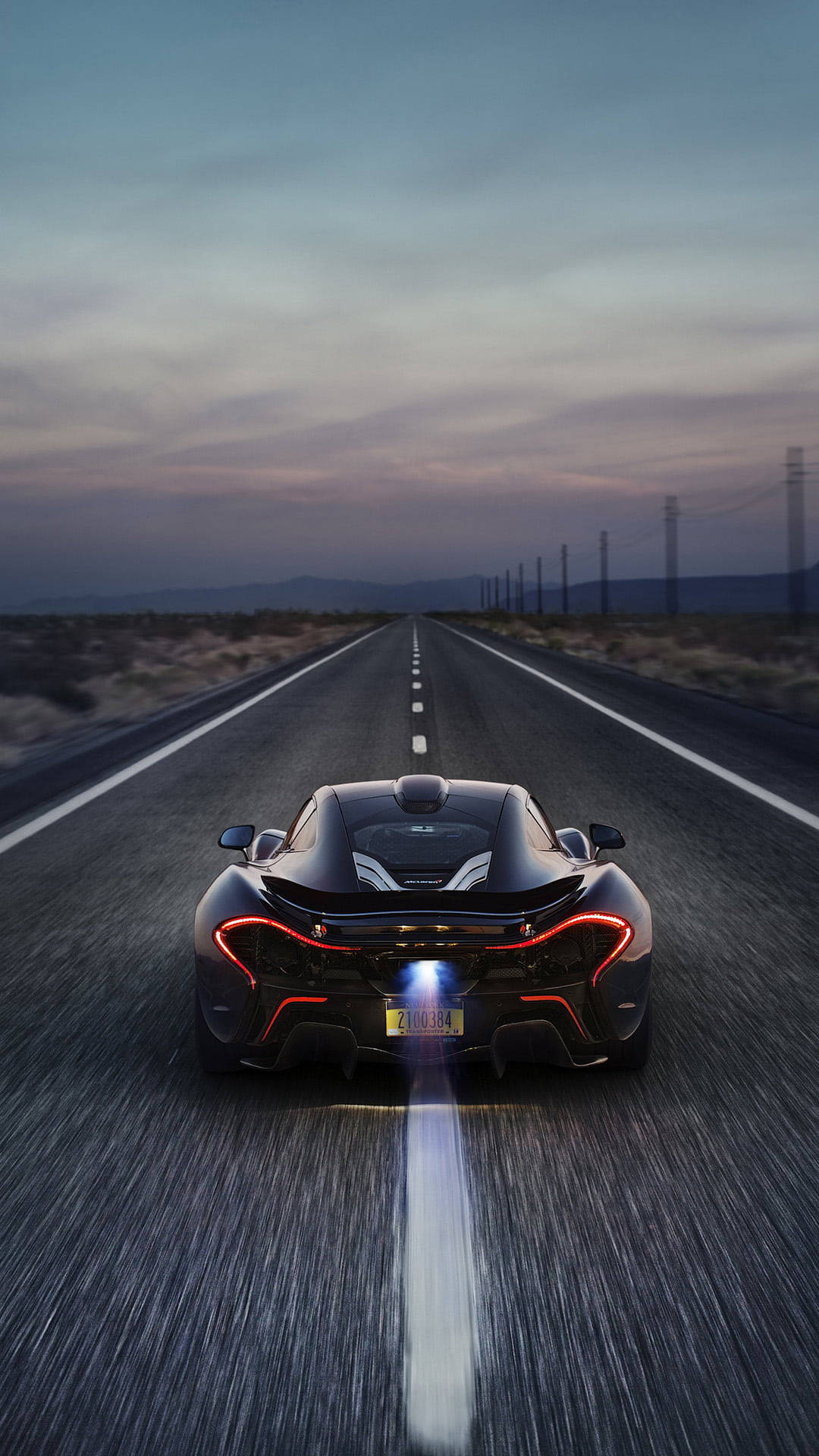 跑車 桌布 壁紙 — 一輛黑色McLaren跑車在黃昏時分沿沙漠高速公路飛馳，尾燈發光並帶有動態模糊效果。
