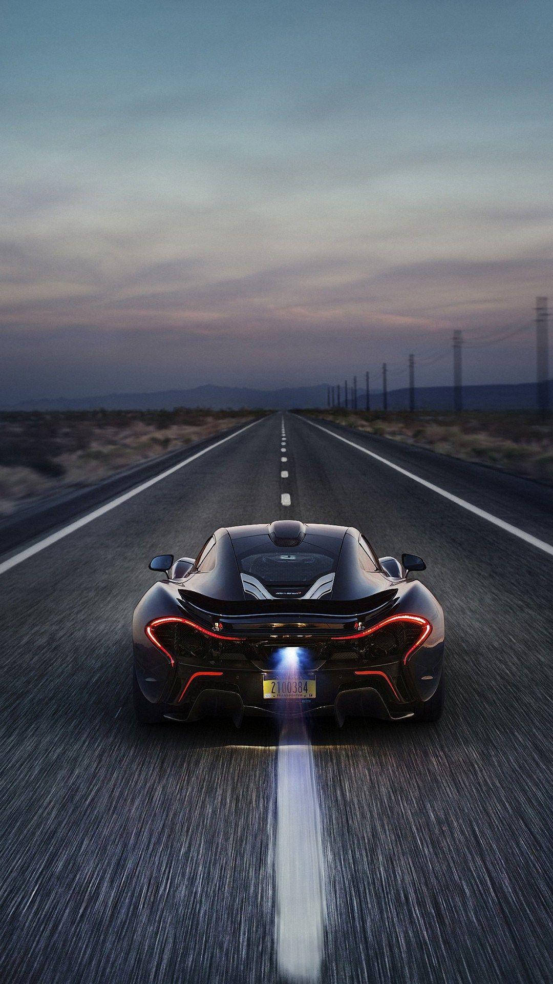 高畫質手機 桌布 壁紙 — 一輛黑色McLaren跑車在黃昏時分在沙漠高速公路上疾馳，帶有發光的紅色尾燈和明亮的排氣痕跡。