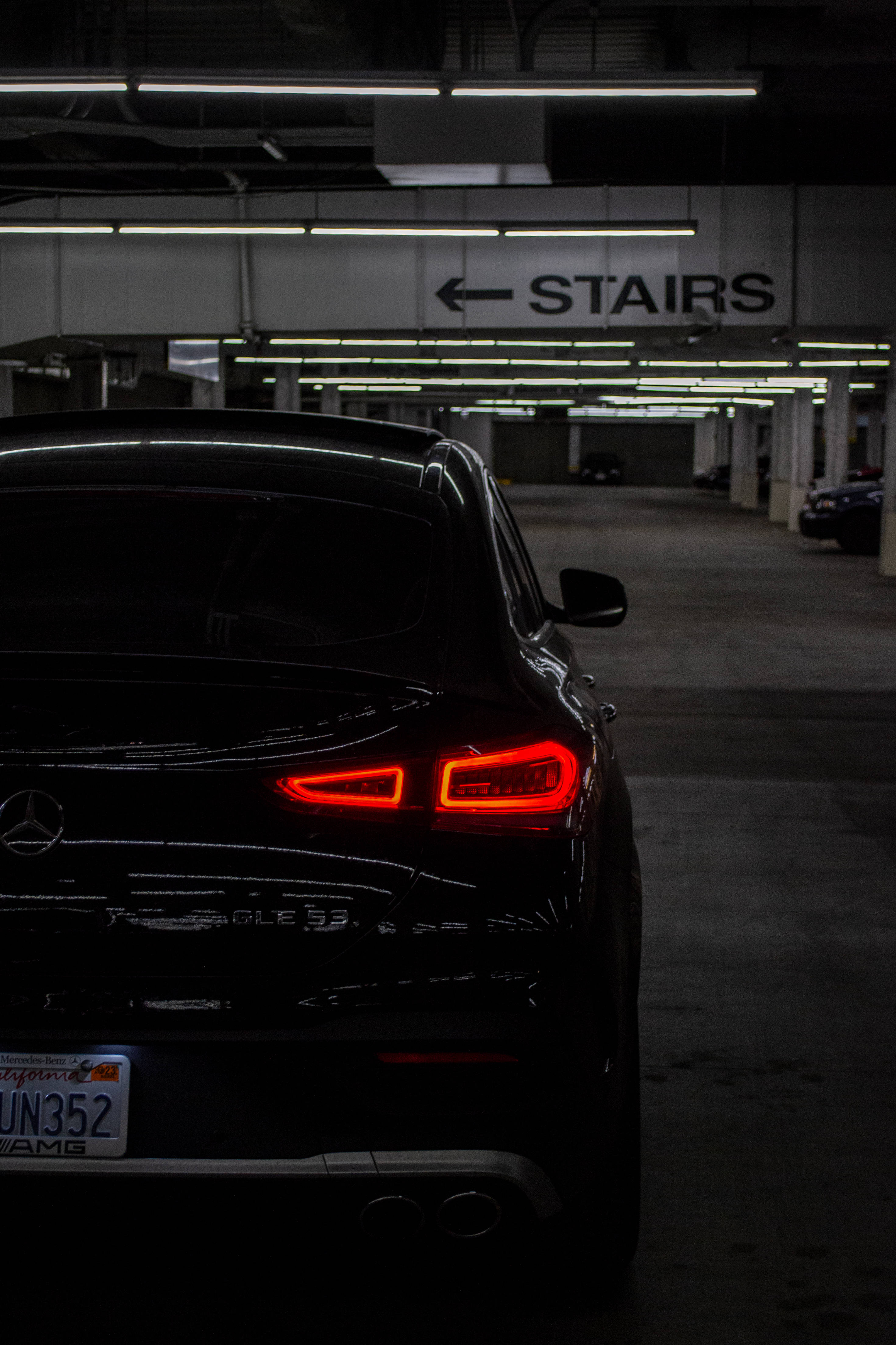 AMG iPhone 桌布 壁紙 — 一輛黑色Mercedes-AMG GLC 63 SUV的發光紅色尾燈在光線昏暗的地下停車場中格外醒目。