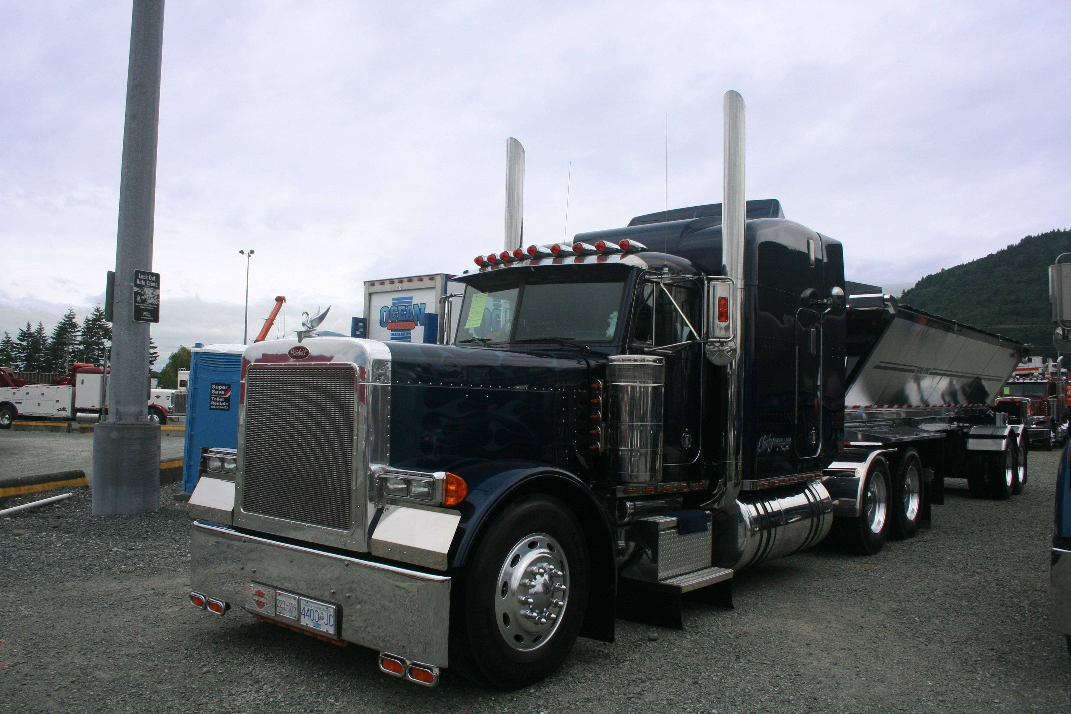 Kenworth W900 桌布 壁紙 — 一輛黑色Peterbilt半掛卡車，帶有鍍鉻裝飾和高排氣管，停在山附近的礫石上。