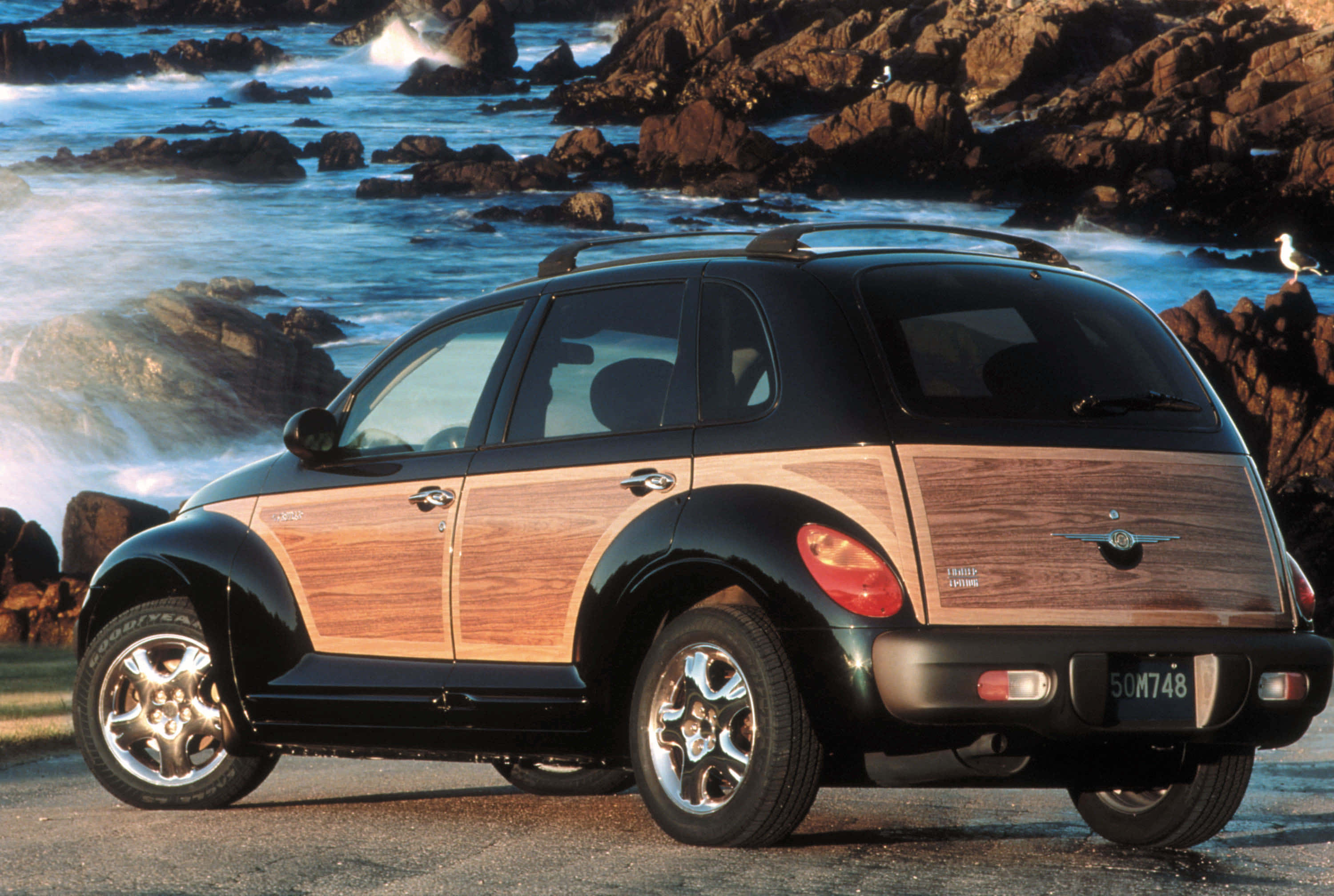 Chrysler Pt Cruiser 桌布 壁紙 — 一輛黑色PT Cruiser配備木質鑲板，停泊在岩石海灘上，海浪拍打著海岸。