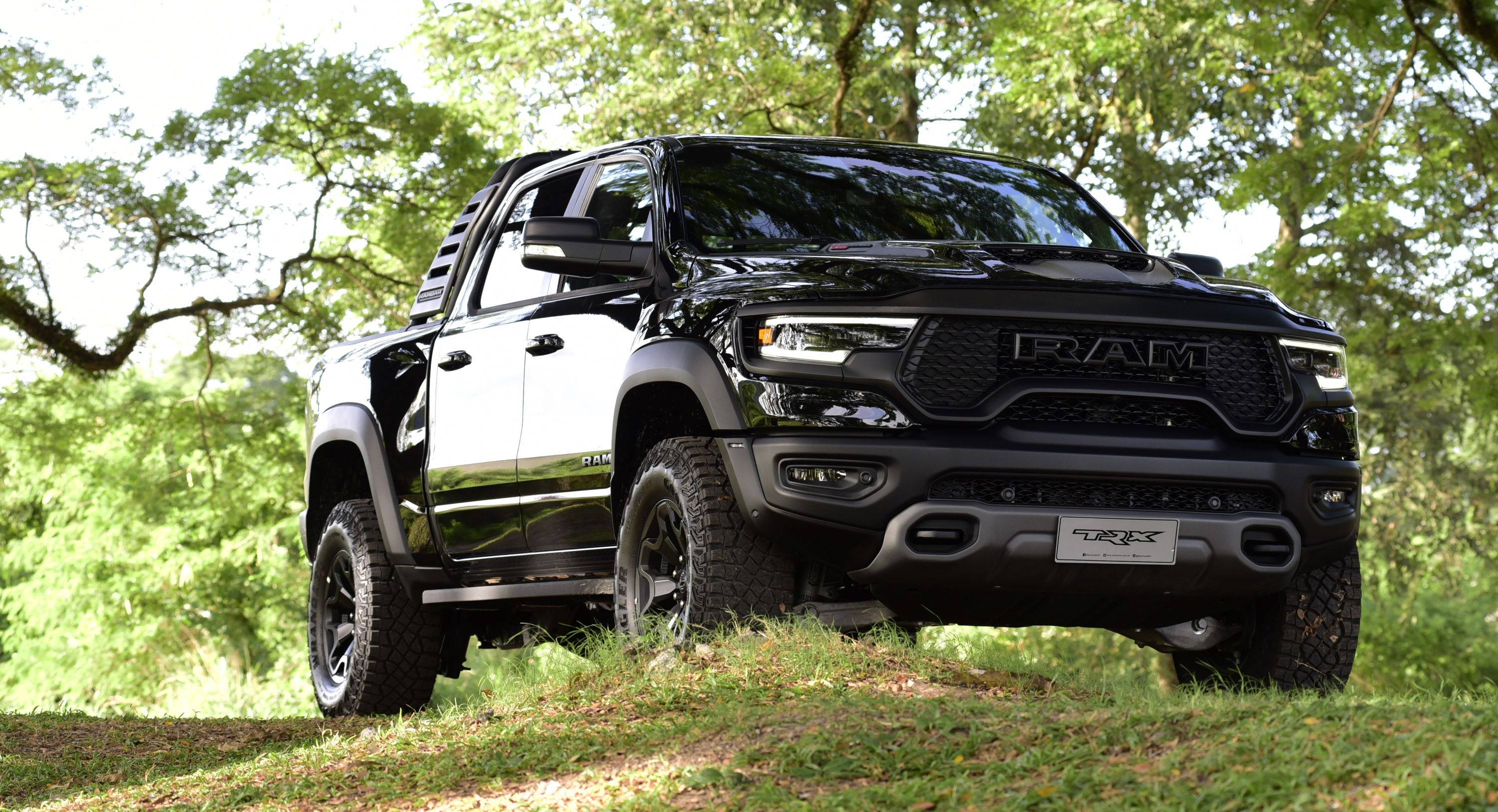 Truck 桌布 壁紙 — 一輛黑色Ram TRX pickup貨車以侵略性造型矗立在長滿青草的山丘上，四周環繞著茂密的綠樹。