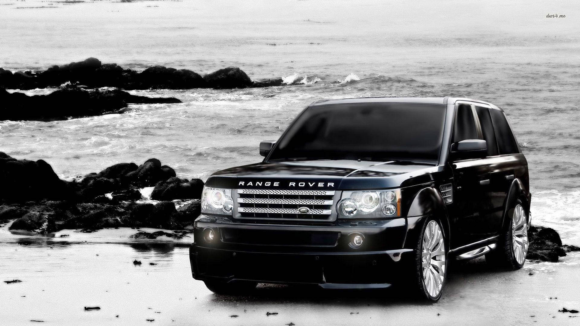 海灘 桌布 壁紙 — 一輛黑色Range Rover SUV停泊在岩石海灘上，海浪拍打岸邊，呈現單色調。