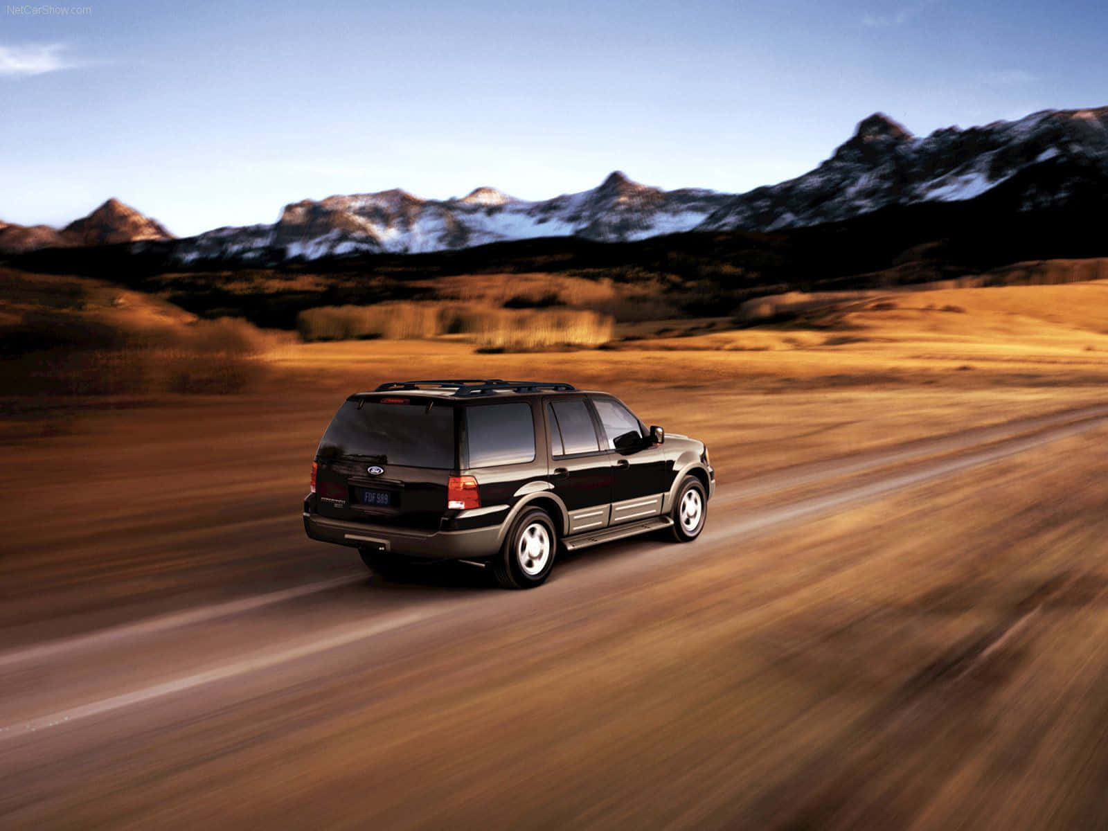 Ford Expedition 桌布 壁紙 — 一輛黑色SUV在沙漠公路上疾駛，背景是白雪覆蓋的山脈，天空晴朗。
