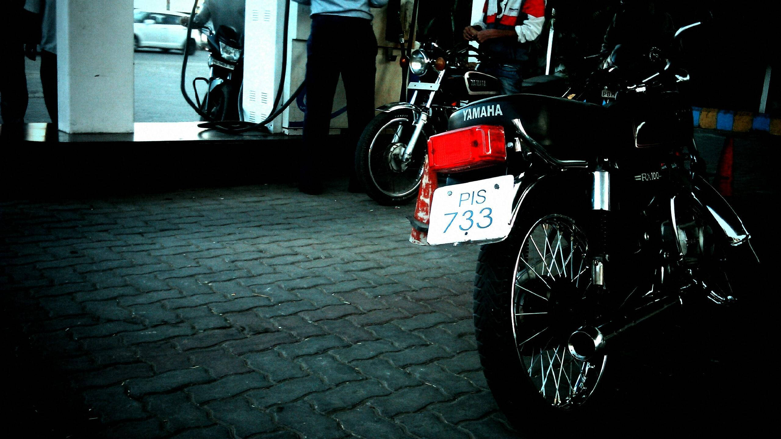 Rx100 桌布 壁紙 — 一輛黑色Yamaha機車，車牌PIS 733，夜晚停泊在鵝卵石街道上，燈光昏暗。