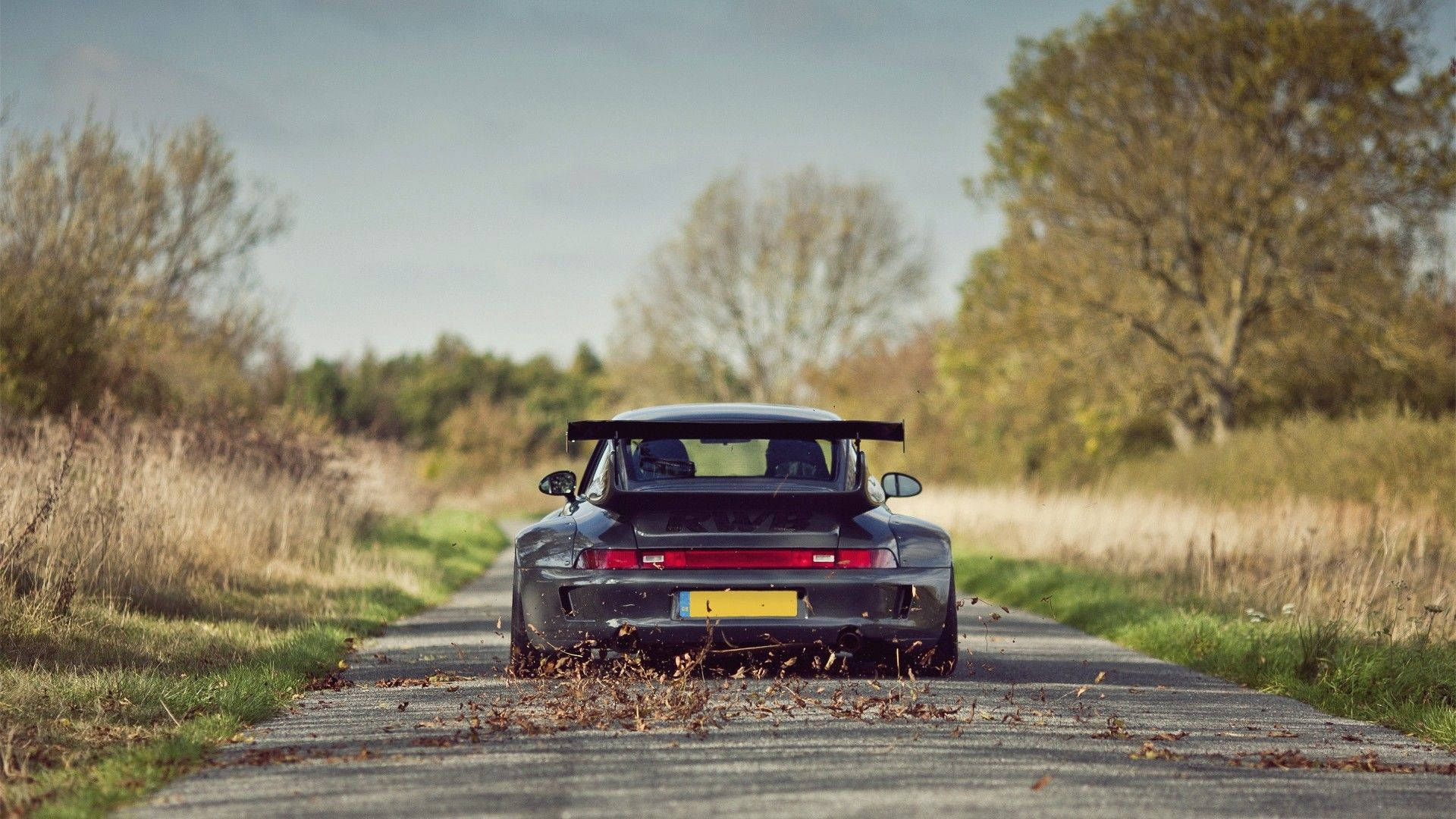 Porsche 911 桌布 壁紙 — 一輛黑色保時捷911 Turbo在鄉村道路上飛馳，在蒼白的天空下揚起秋天的落葉。
