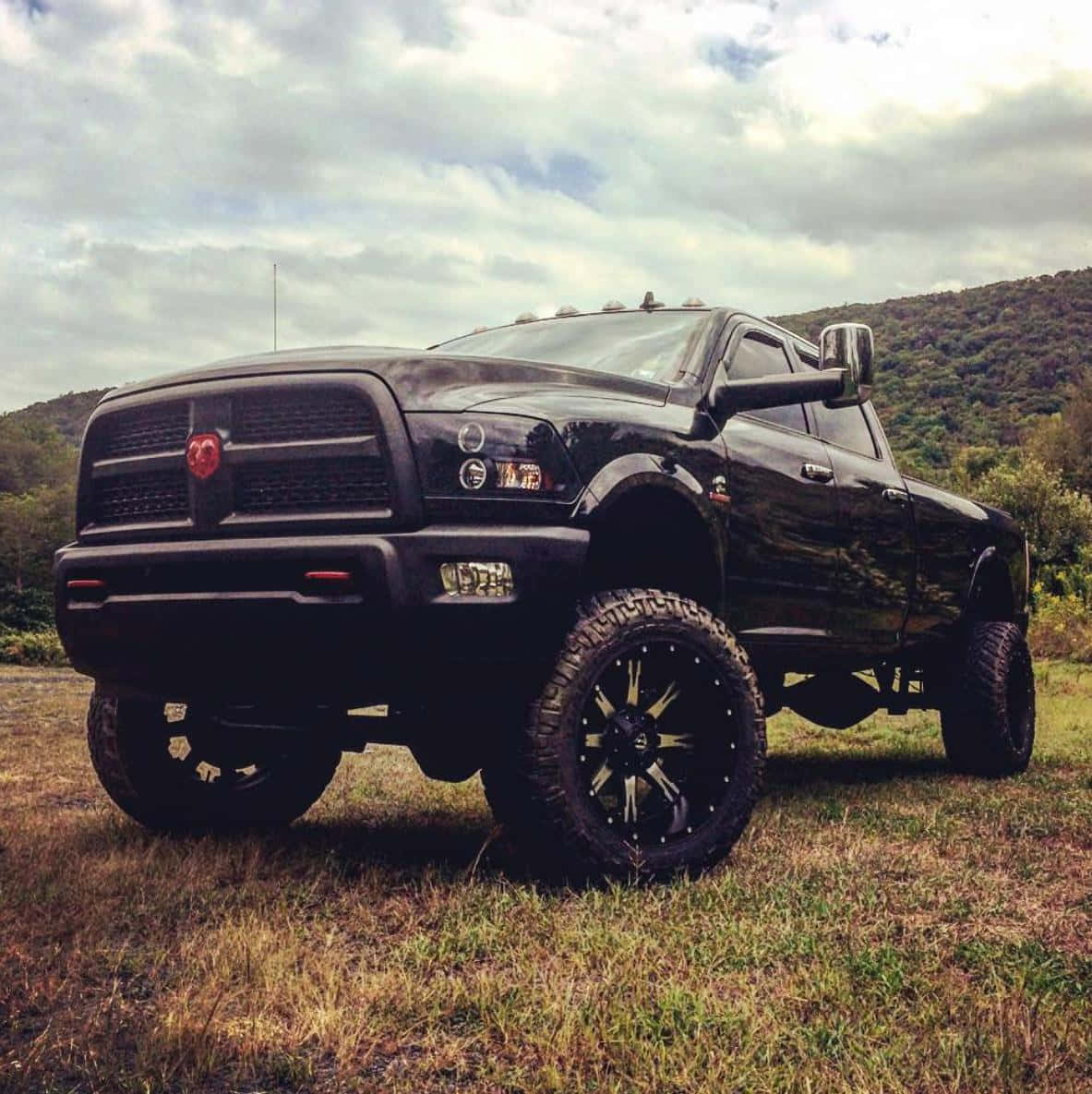 Jacked Up Trucks 桌布 壁紙 — 一輛黑色升高的Ram卡車配備大型越野輪胎，在陰天天空下自豪地矗立在草地上。