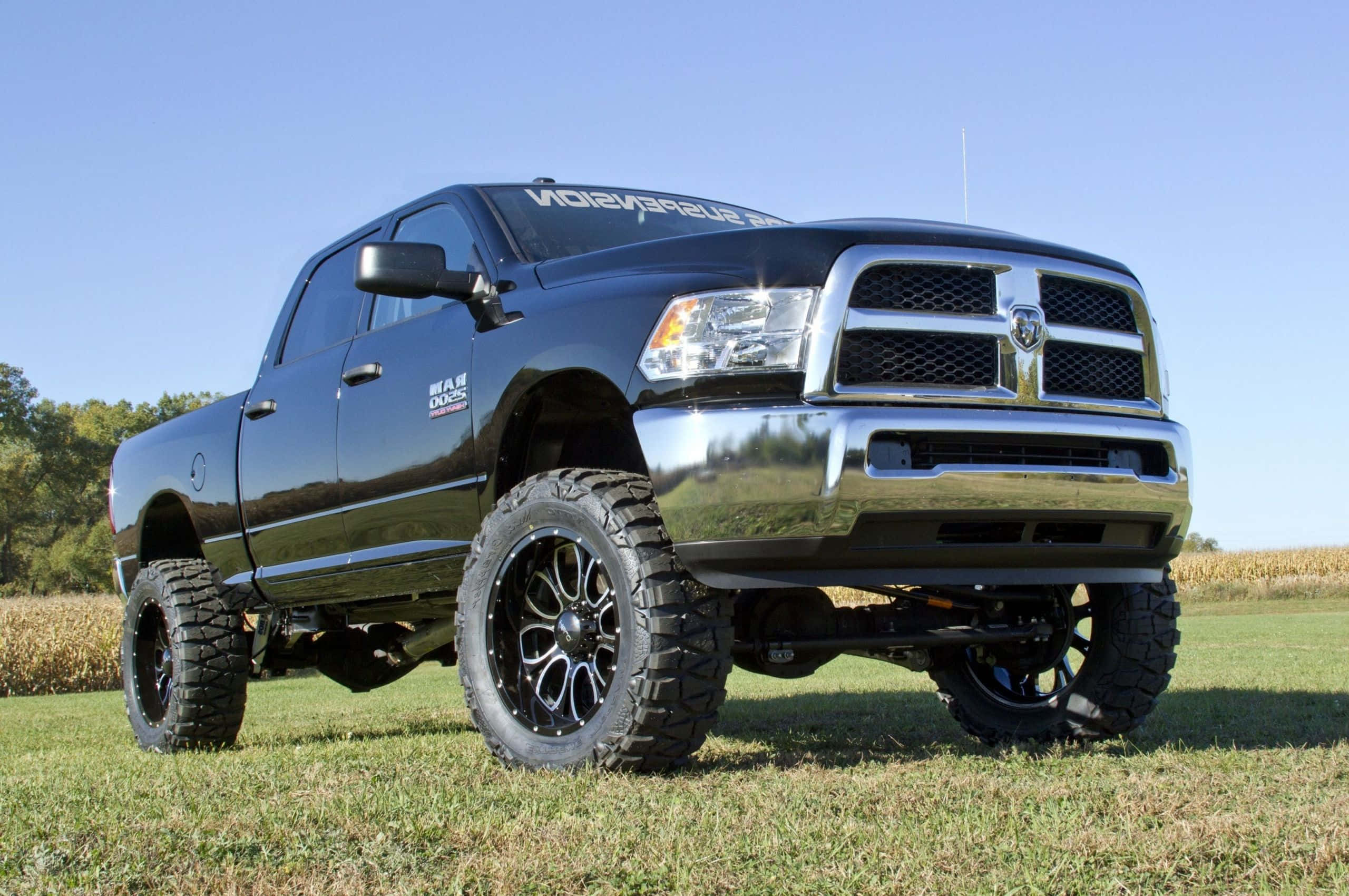 Jacked Up Trucks 桌布 壁紙 — 一輛黑色升高的Ram皮卡車，配備大型越野輪胎，在晴朗藍天下的草地上自豪地站立。