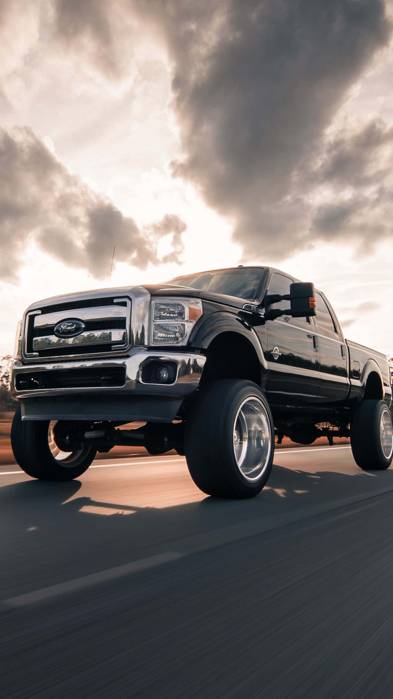 Lifted Truck 桌布 壁紙 — 一輛黑色升高的福特F-150 pickup truck在戲劇性的多雲日落天空下在高速公路上飛馳。