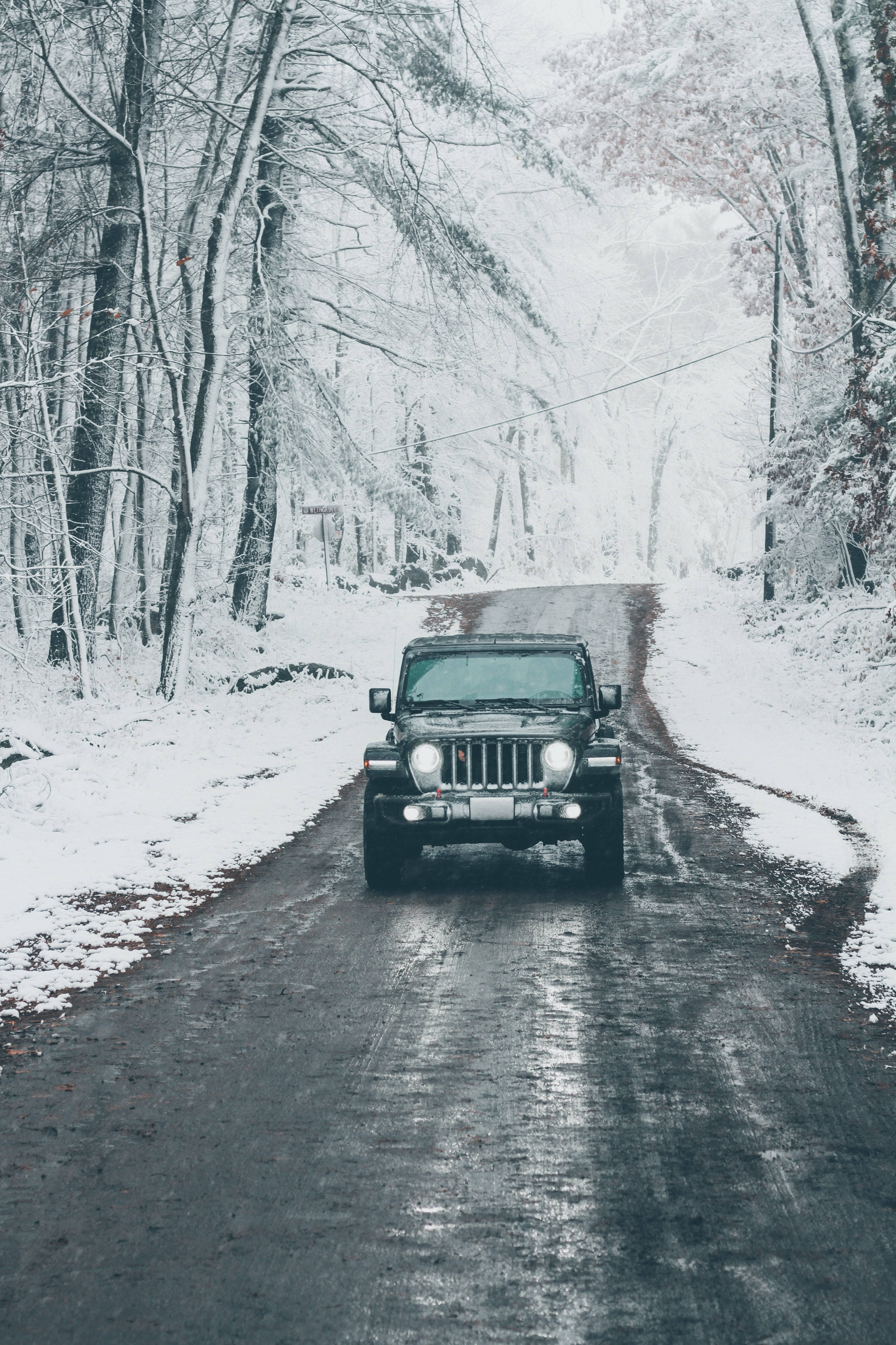 黑色吉普車 桌布 壁紙 — 一輛黑色吉普車在灰色冬日天空下行駛在積雪的森林道路上。