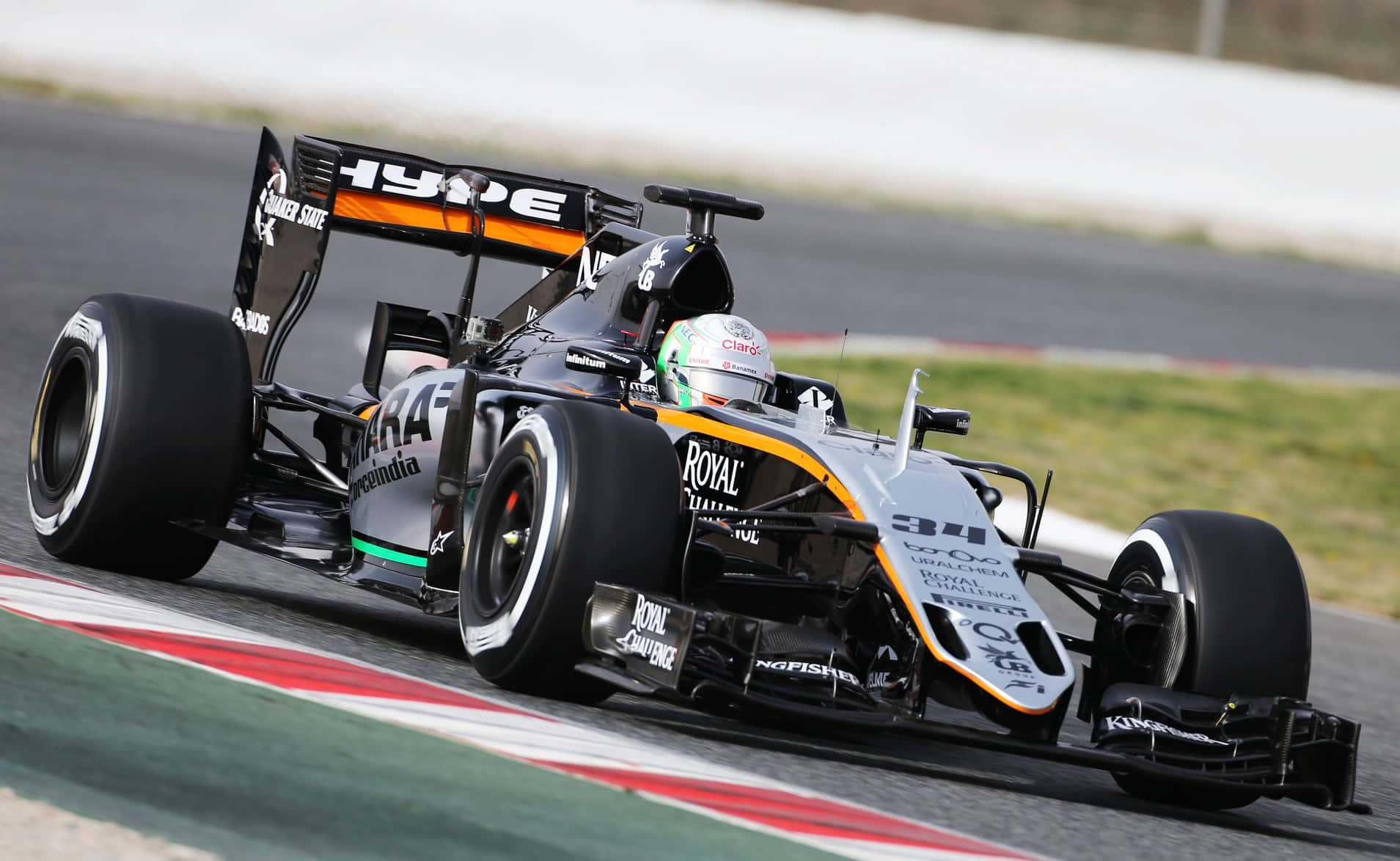 HD F1 2016 桌布 壁紙 — 一輛黑色和橙色的 Formula 1 賽車，編號 34，沿著一條以紅、白、綠色路緣石為邊界的賽道疾馳。