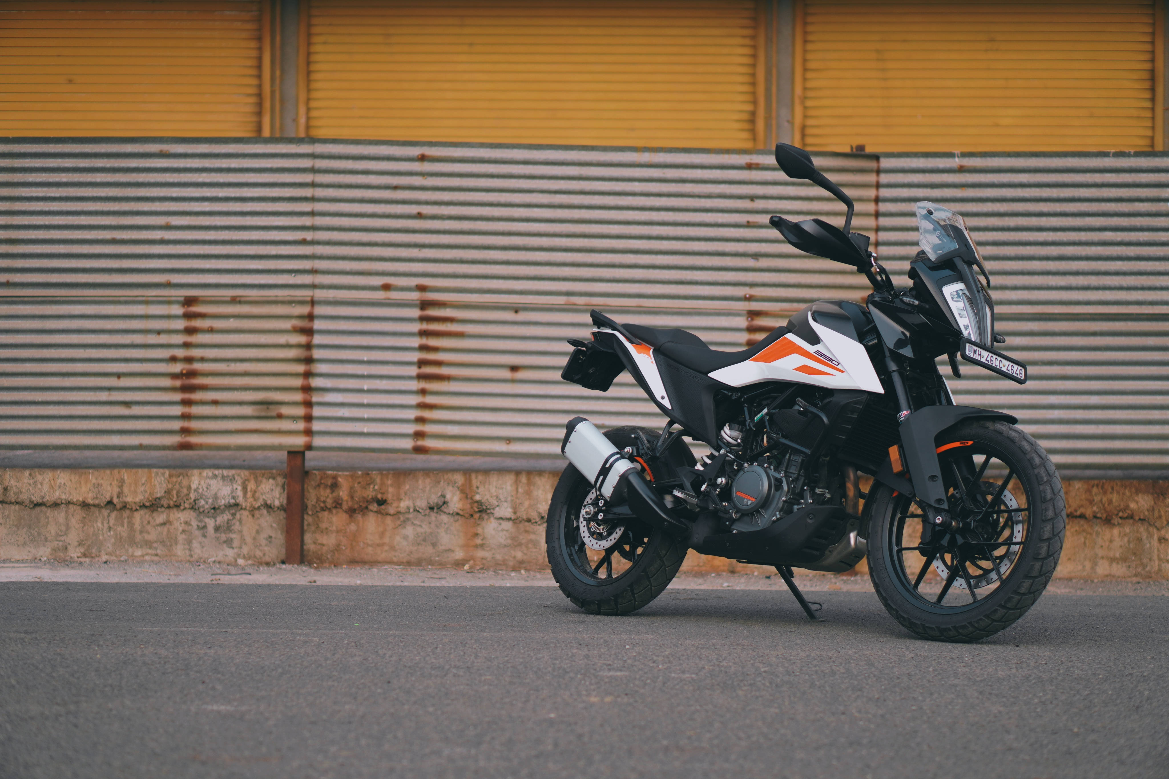 Ktm Bike 桌布 壁紙 — 一輛黑色和橙色的冒險摩托車停在瀝青路上，背景是帶有鏽跡的風化波紋金屬牆。