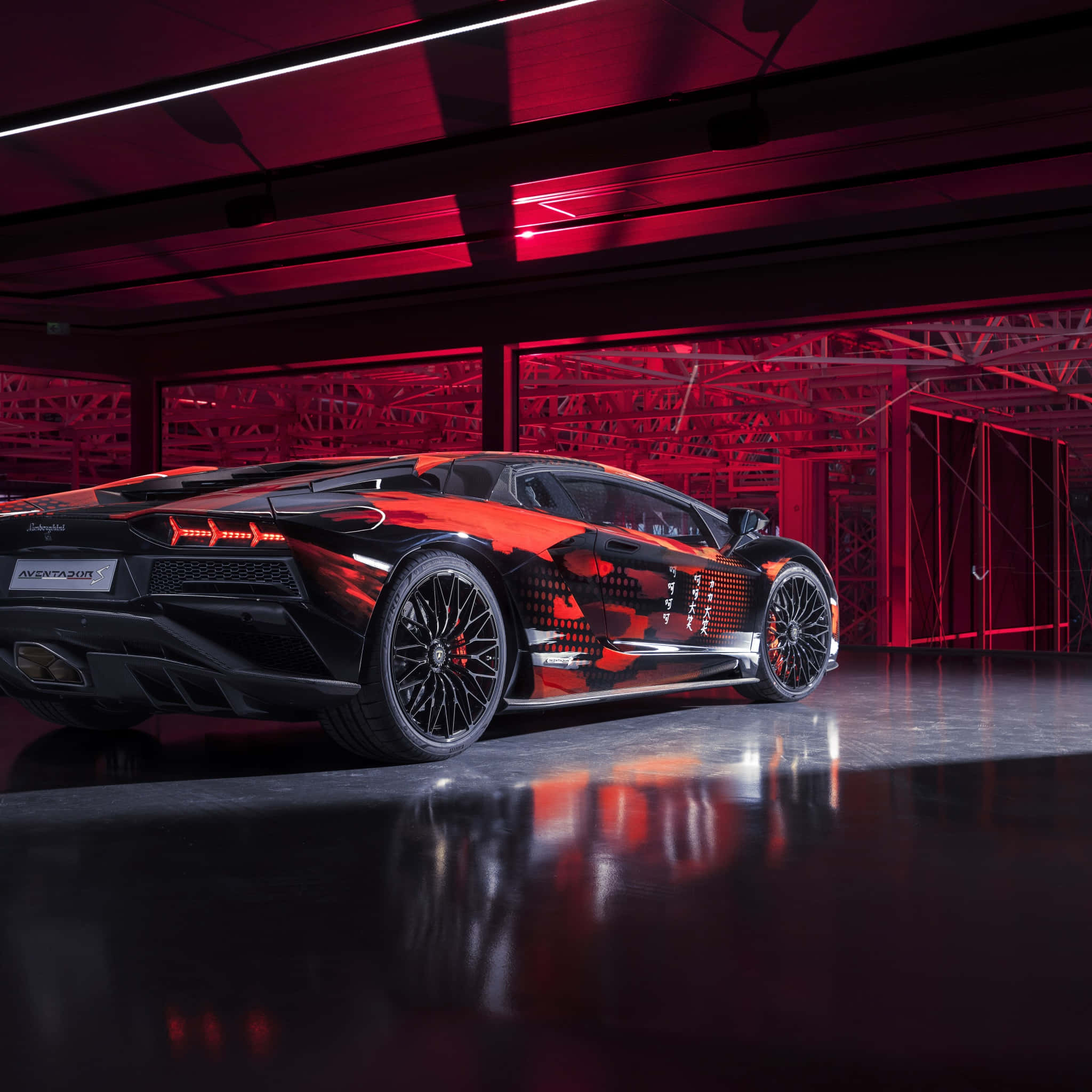 手機 桌布 壁紙 — 一輛黑色和紅色的藍寶堅尼 Aventador SVJ，側面有日文字，停在紅色燈光的工業車庫中，地板有反射效果。
