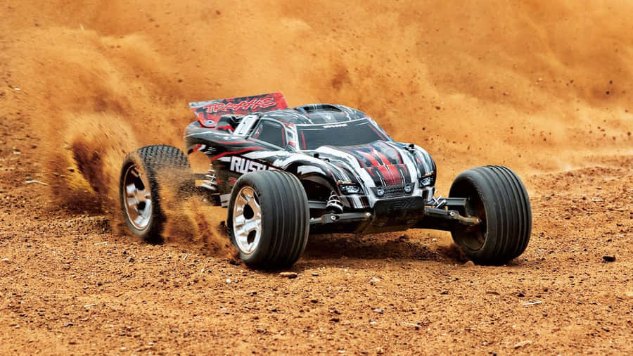 Rc Cars 桌布 壁紙 — 一輛黑色和紅色的遙控怪獸卡車在泥土賽道上疾馳，揚起橙色塵土。