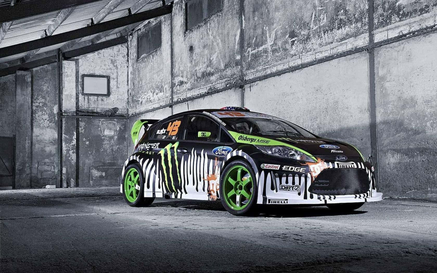 Ford Fiesta 桌布 壁紙 — 一輛黑色和綠色的Monster Energy福特拉力賽車，帶有斑馬條紋，停放在骯髒的工業倉庫中。