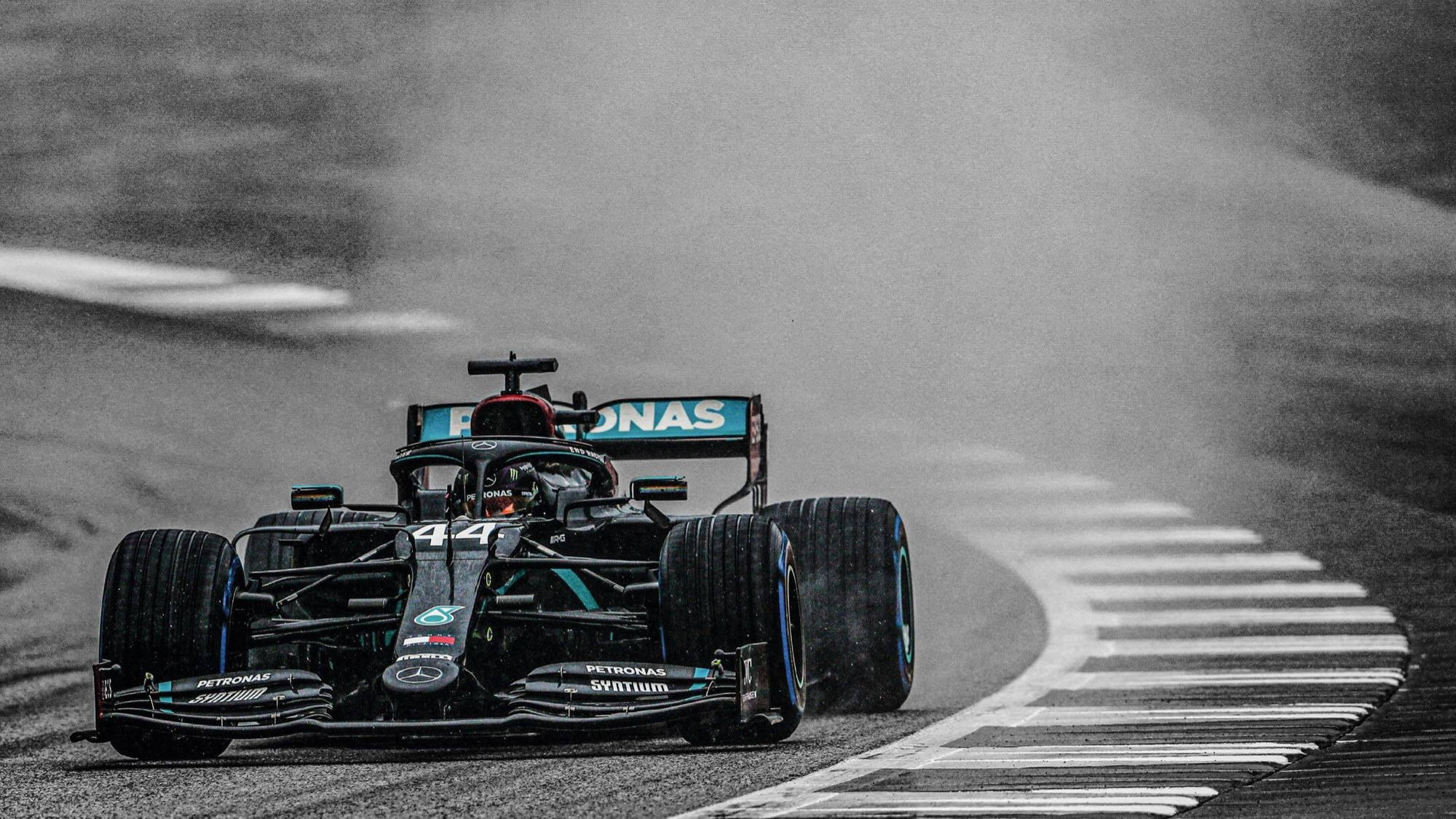 F1 桌布 壁紙 — 一輛黑色和藍綠色的44號一級方程式賽車在賽道的濕滑彎道上疾馳，輪胎噴出水霧。