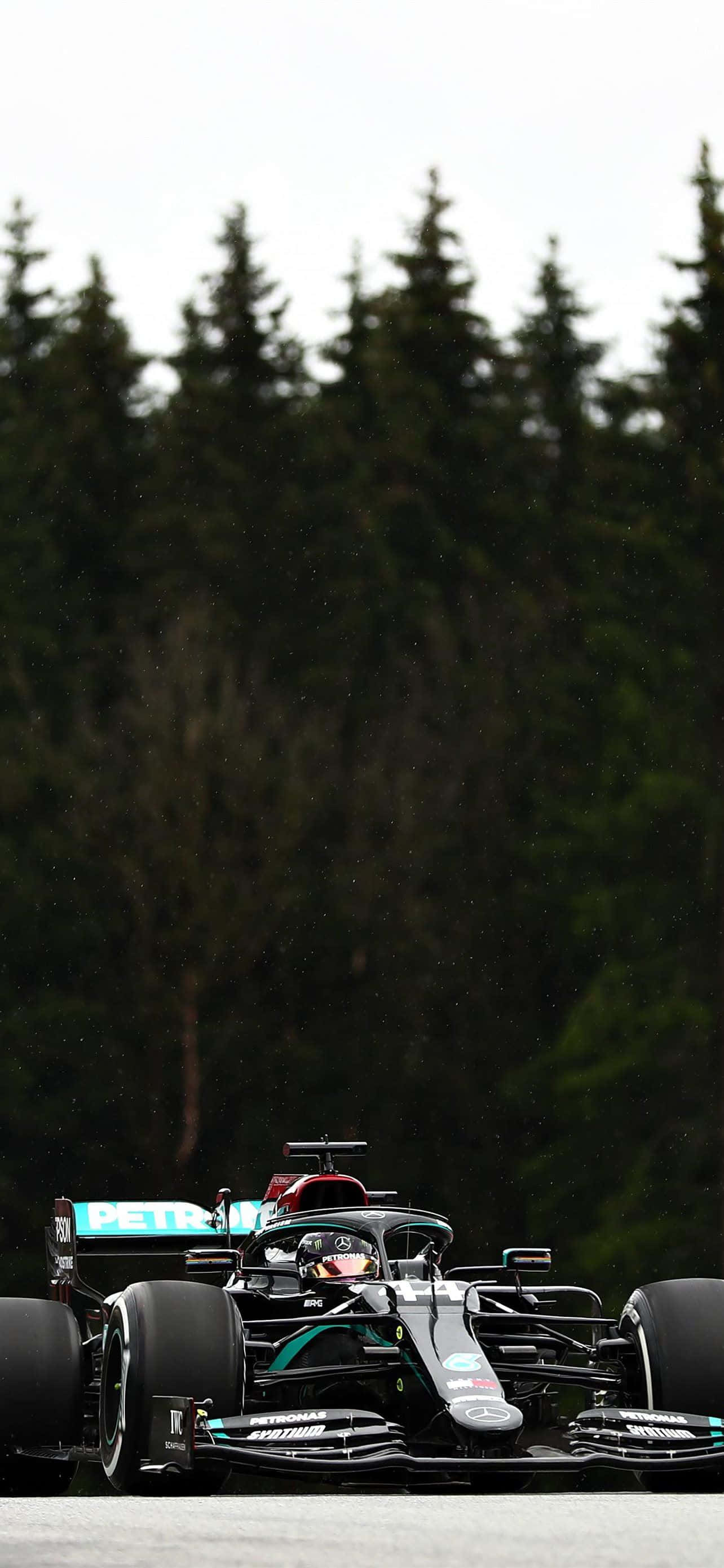 Formula 1 iPhone 桌布 壁紙 — 一輛黑色和藍綠色的F1賽車在潮濕的賽道上疾馳，背景是茂密的森林，天空多雲。