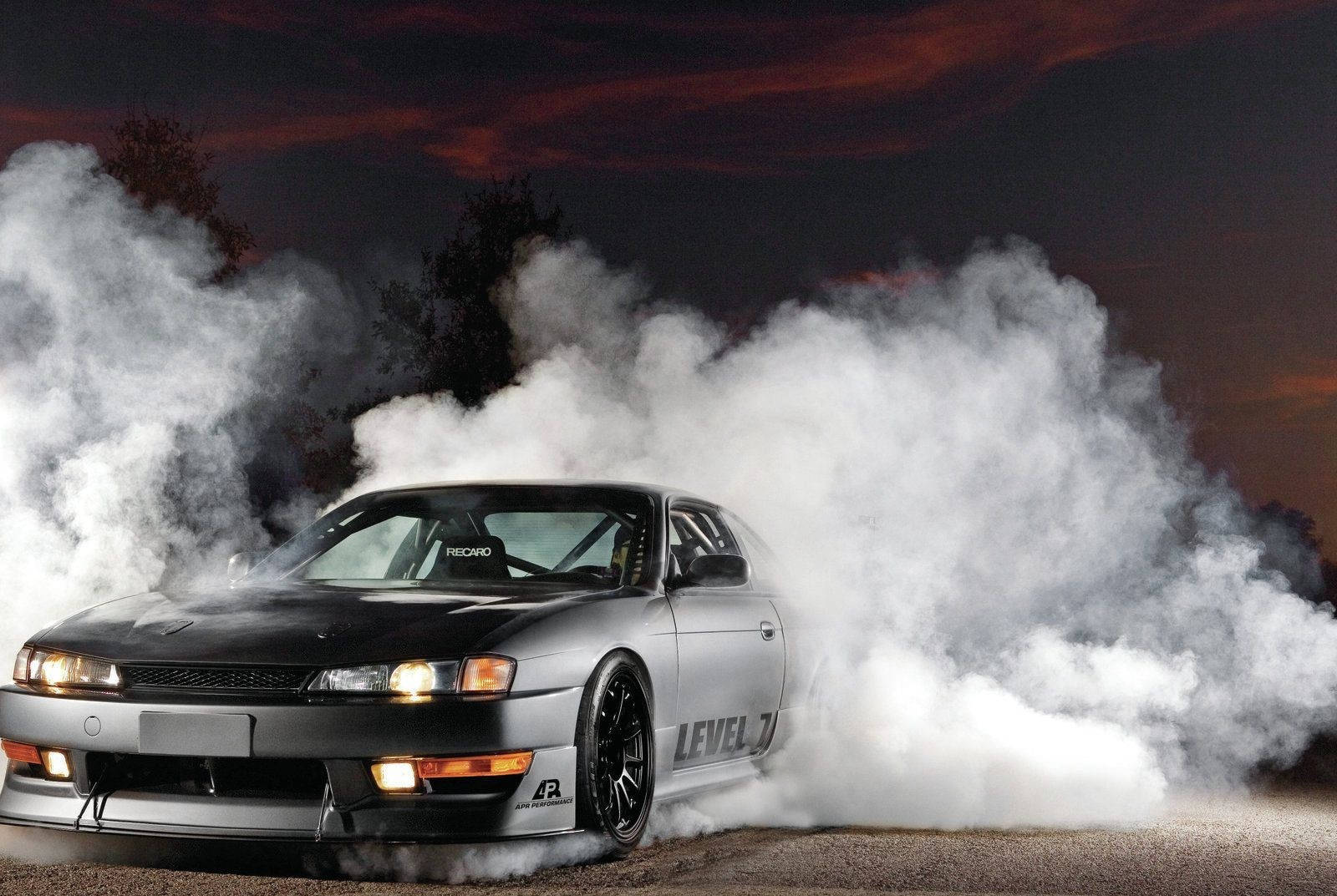 Nissan Silvia S14 桌布 壁紙 — 一輛黑色和銀色的跑車在夜間飄移，揚起濃厚的白煙，映襯著火橙色和黑暗的天空。