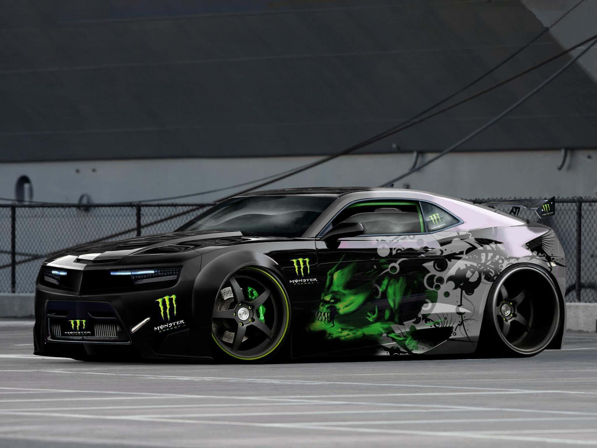 Modified Car 桌布 壁紙 — 一輛黑色和銀色的雪佛蘭Camaro，帶有發光的綠色Monster Energy骷髏圖案，停在工業區。
