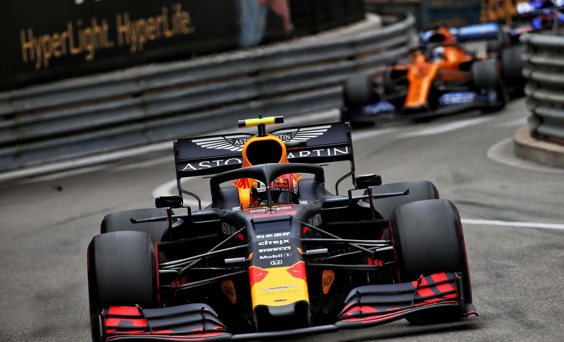 Max Verstappen 桌布 壁紙 — 一輛黑色和黃色的Aston Martin一級方程式賽車在潮濕的賽道上緊密競賽，後面可見另一輛橙色賽車。