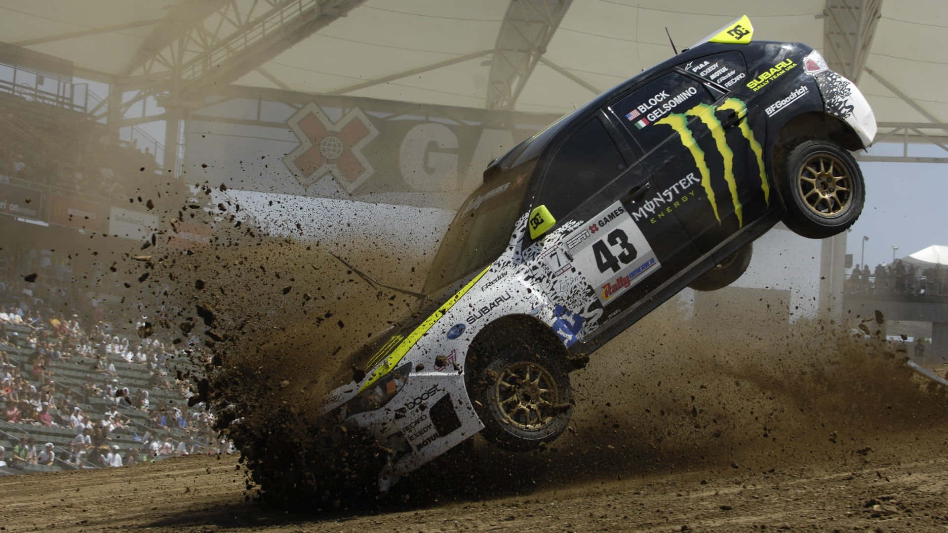1920x1080 Dirt Rally 桌布 壁紙 — 一輛黑色和黃色的拉力賽車（編號43）在泥地賽道上空飛翔，噴灑泥漿，觀眾在看台上觀看。