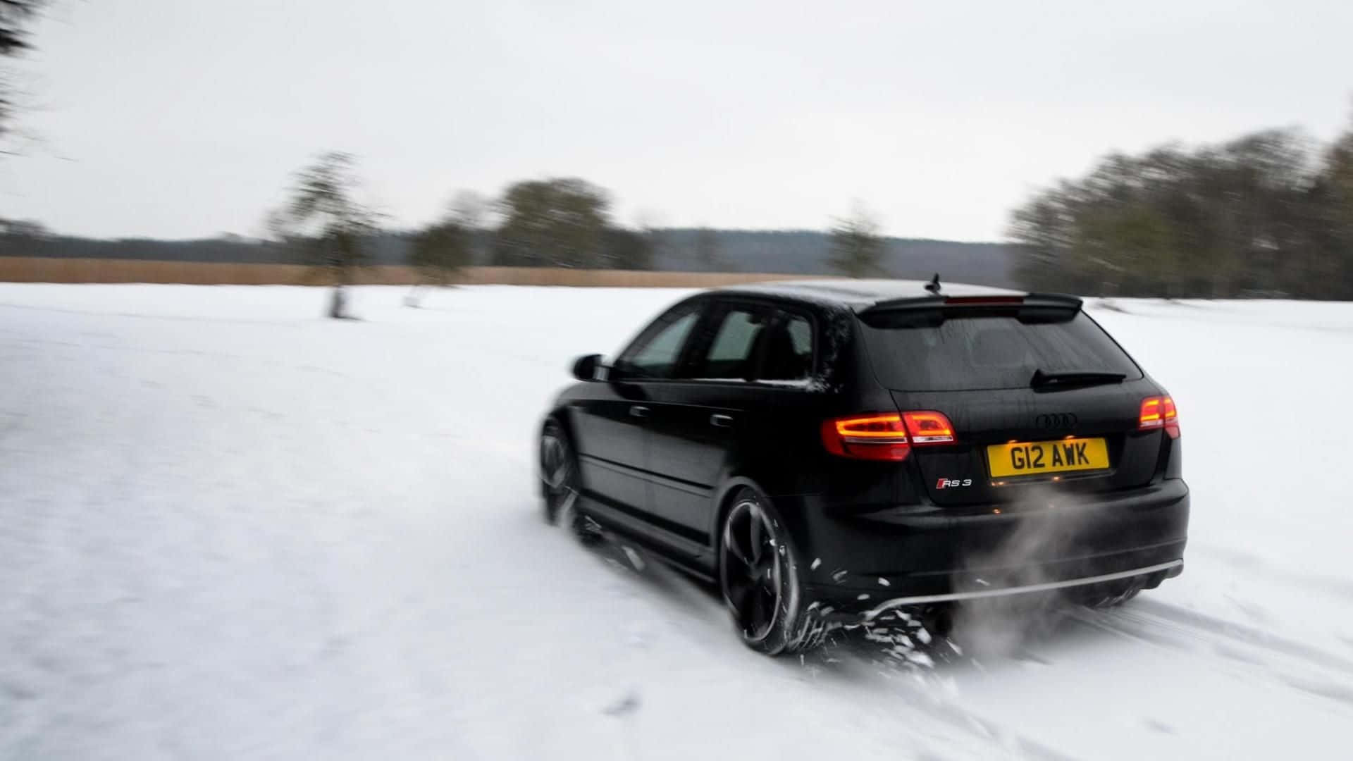 Audi Rs3 桌布 壁紙 — 一輛黑色奧迪RS3旅行車在雪地中疾馳，揚起雪花，背景是模糊的樹木。