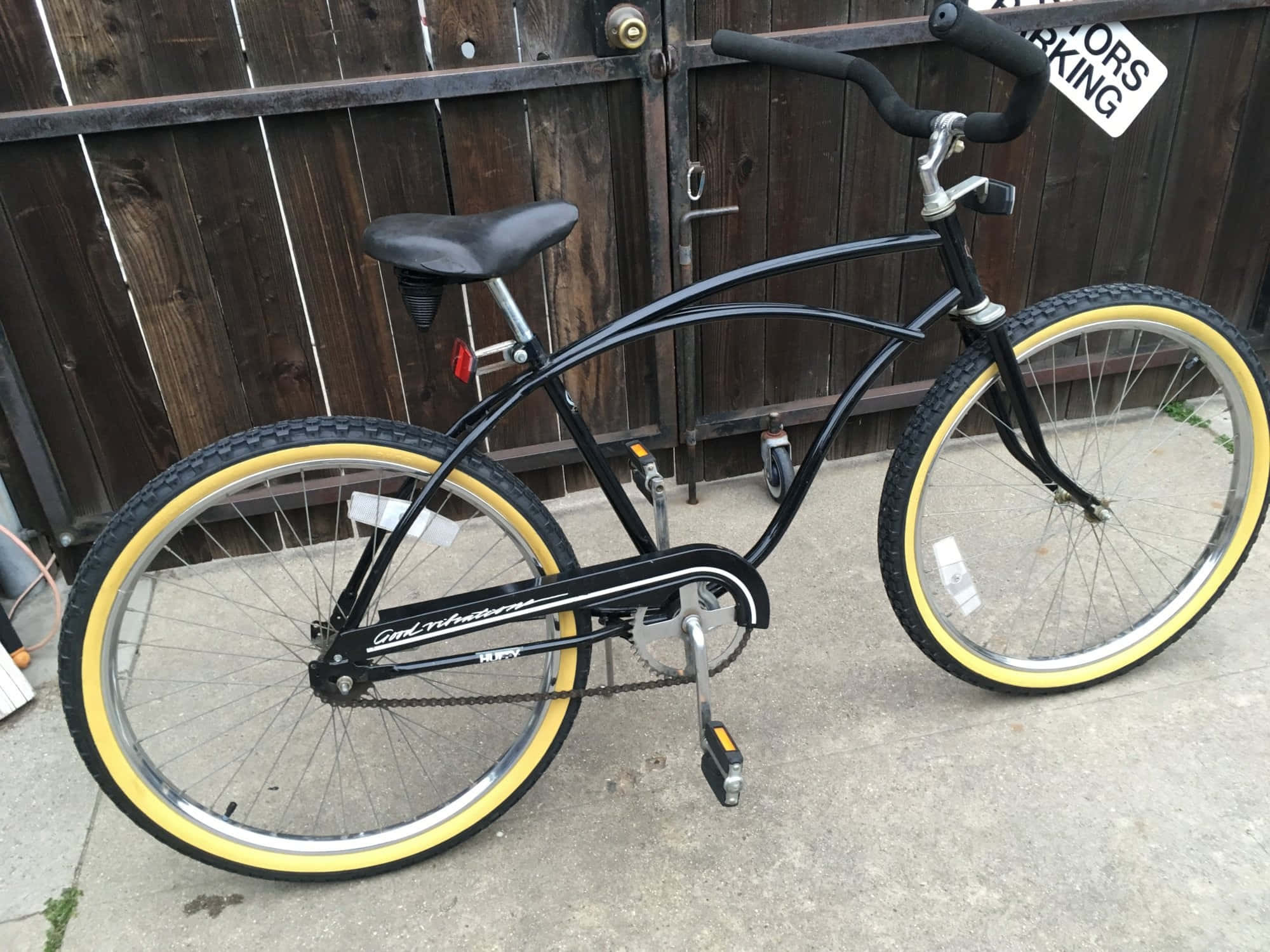 Beach Cruiser 桌布 壁紙 — 一輛黑色巡航自行車搭配亮黃色輪胎，靠在混凝土庭院中經風化的木柵欄上。