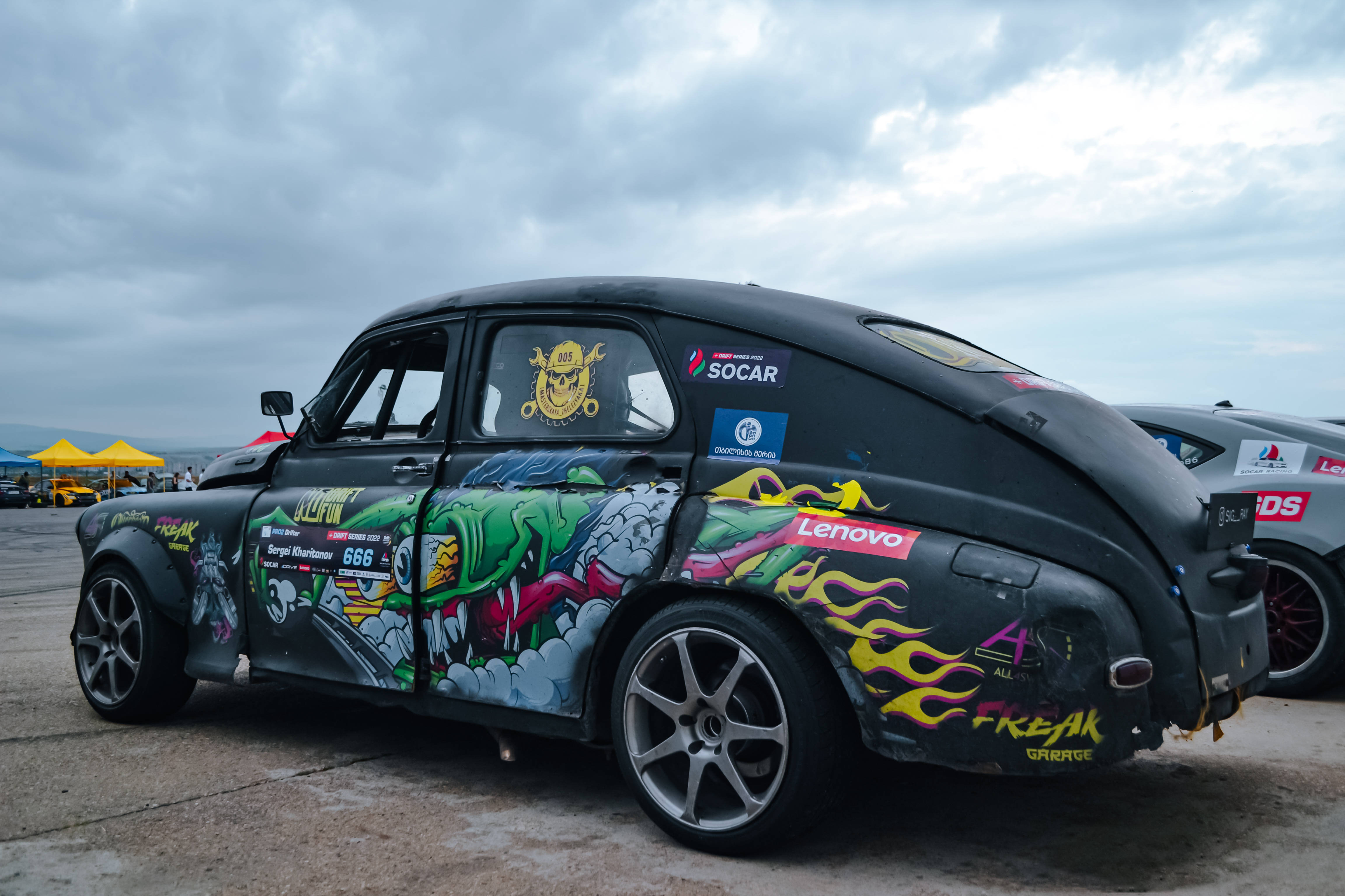 Racing 桌布 壁紙 — 一輛黑色復古直線加速賽車，帶有鮮豔的塗鴉藝術和贊助商貼紙，停泊在陰天的賽道上。
