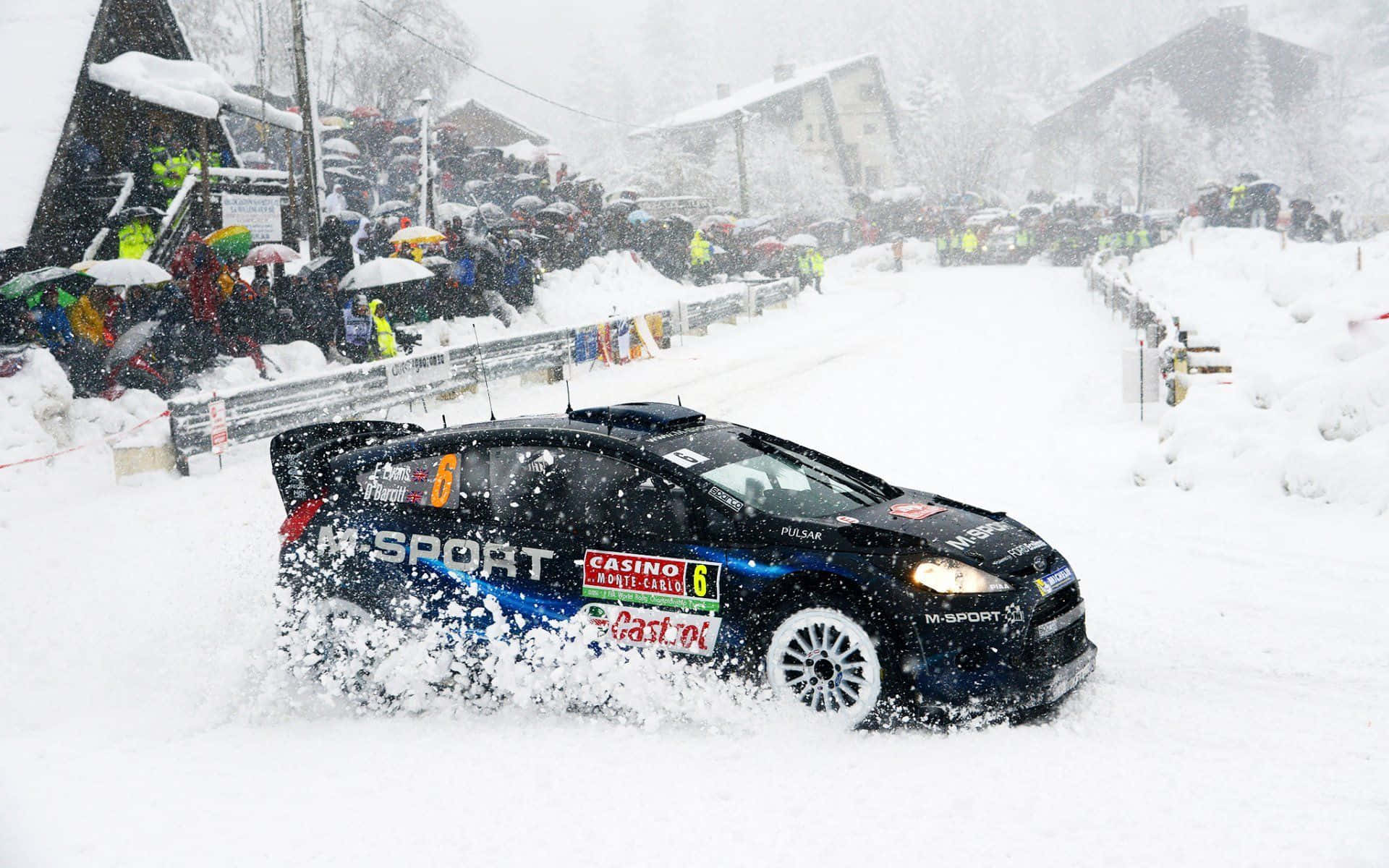 Ice Racing 桌布 壁紙 — 一輛黑色拉力賽車在積雪的山村街道上飛馳，揚起雪花，街道兩旁站滿觀眾。