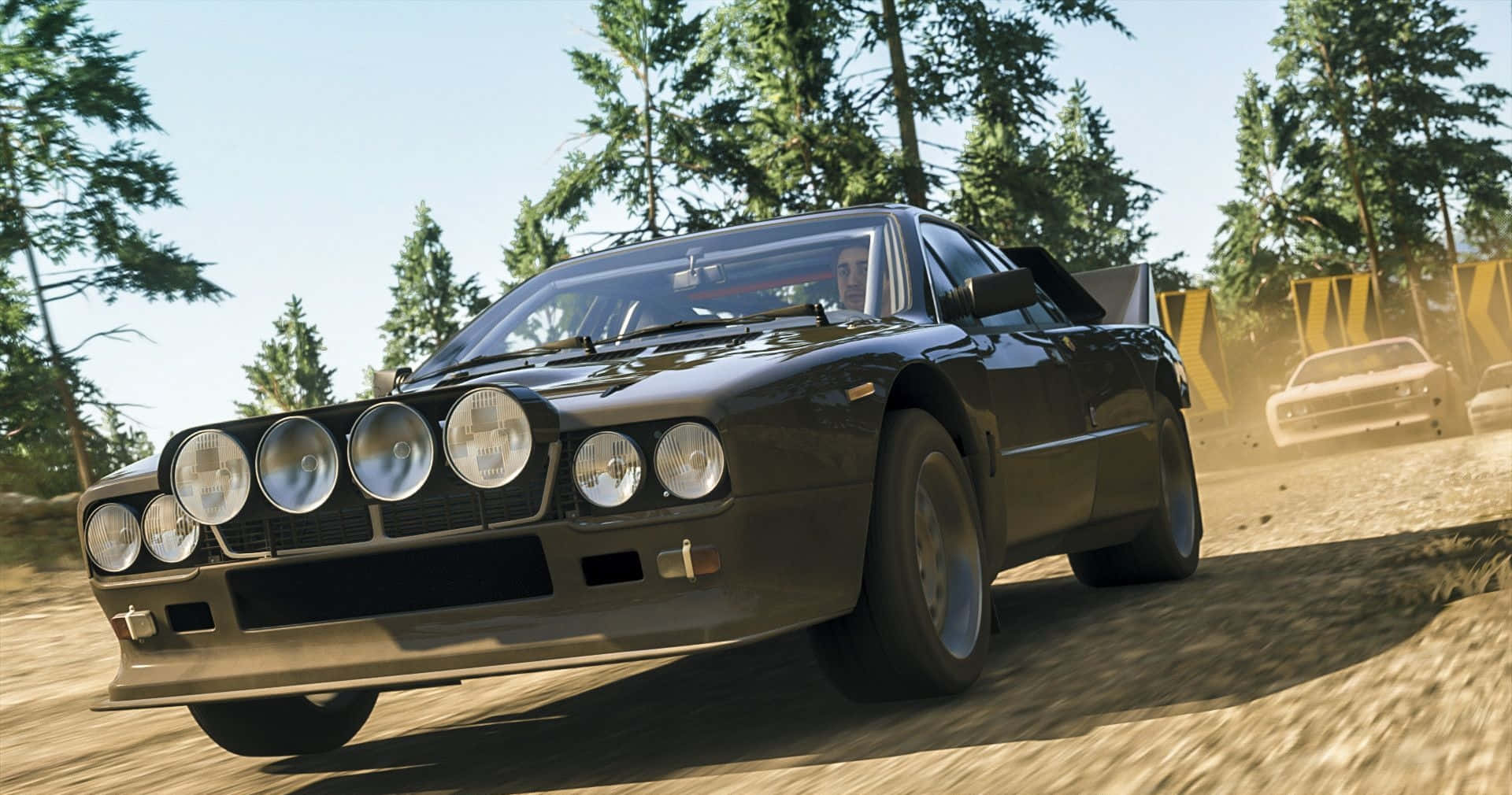 Lancia 桌布 壁紙 — 一輛黑色拉力賽車配備六個圓形頭燈，在塵土飛揚的森林賽道上疾馳，背景有松樹和另一輛賽車。