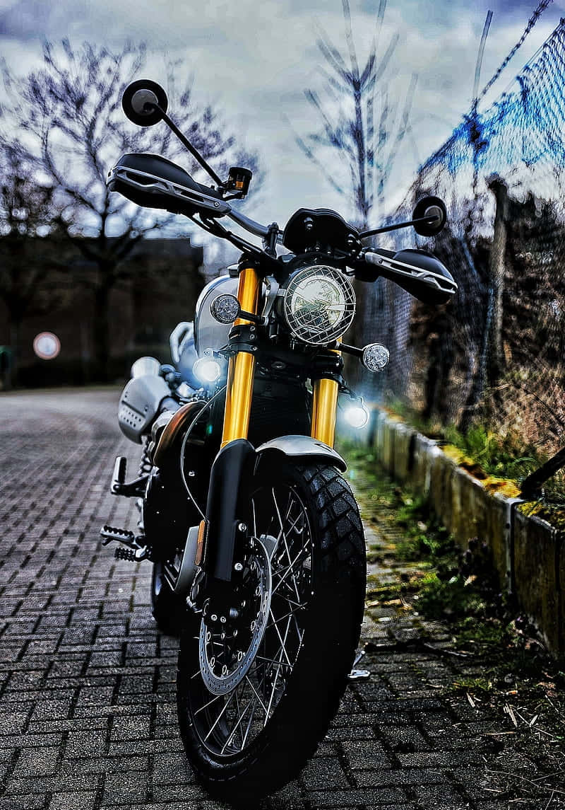 Superbike 桌布 壁紙 — 一輛黑色摩托車搭配金色前叉，停在陰天下的鵝卵石小徑上。