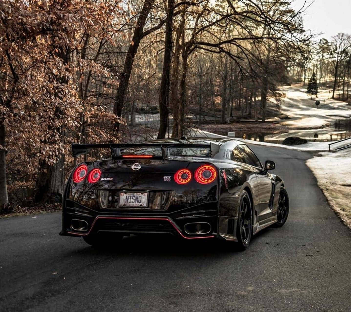 Nissan 桌布 壁紙 — 一輛黑色日產GT-R，帶有發光的紅色尾燈，停在一條蜿蜒的林間道路上，周圍是光禿禿的樹木。