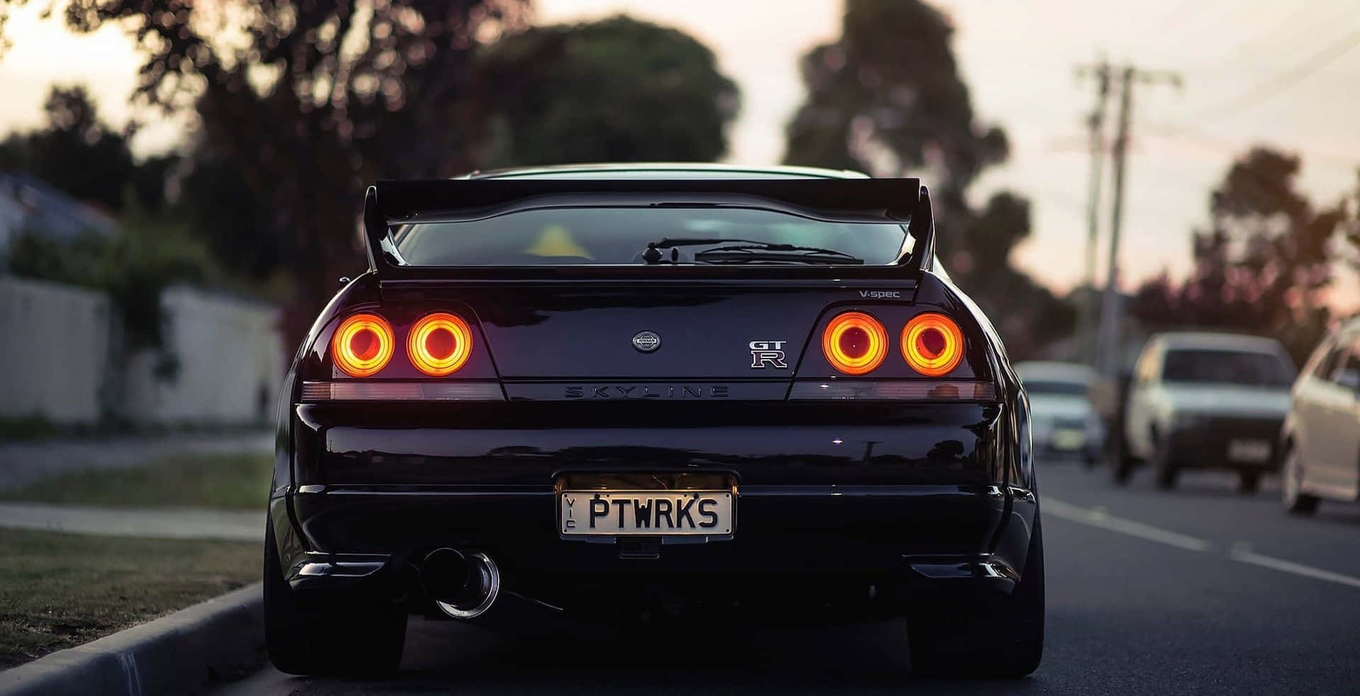 R33 GT-R 桌布 壁紙 — 一輛黑色日產Skyline GT-R，帶有發光的橙色尾燈，停在日落時分的郊區街道上。