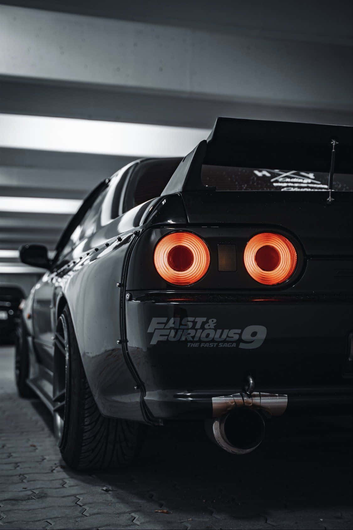 電影動圖 桌布 壁紙 — 一輛黑色日產Skyline R34，帶有發光的橙色圓形尾燈，停在光線昏暗的地下車庫中。