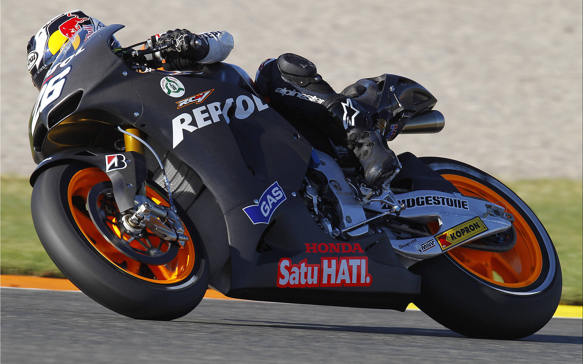 Racing 桌布 壁紙 — 一輛黑色本田MotoGP機車配橙色輪胎，在賽道上急彎時車手身穿Red Bull裝備。