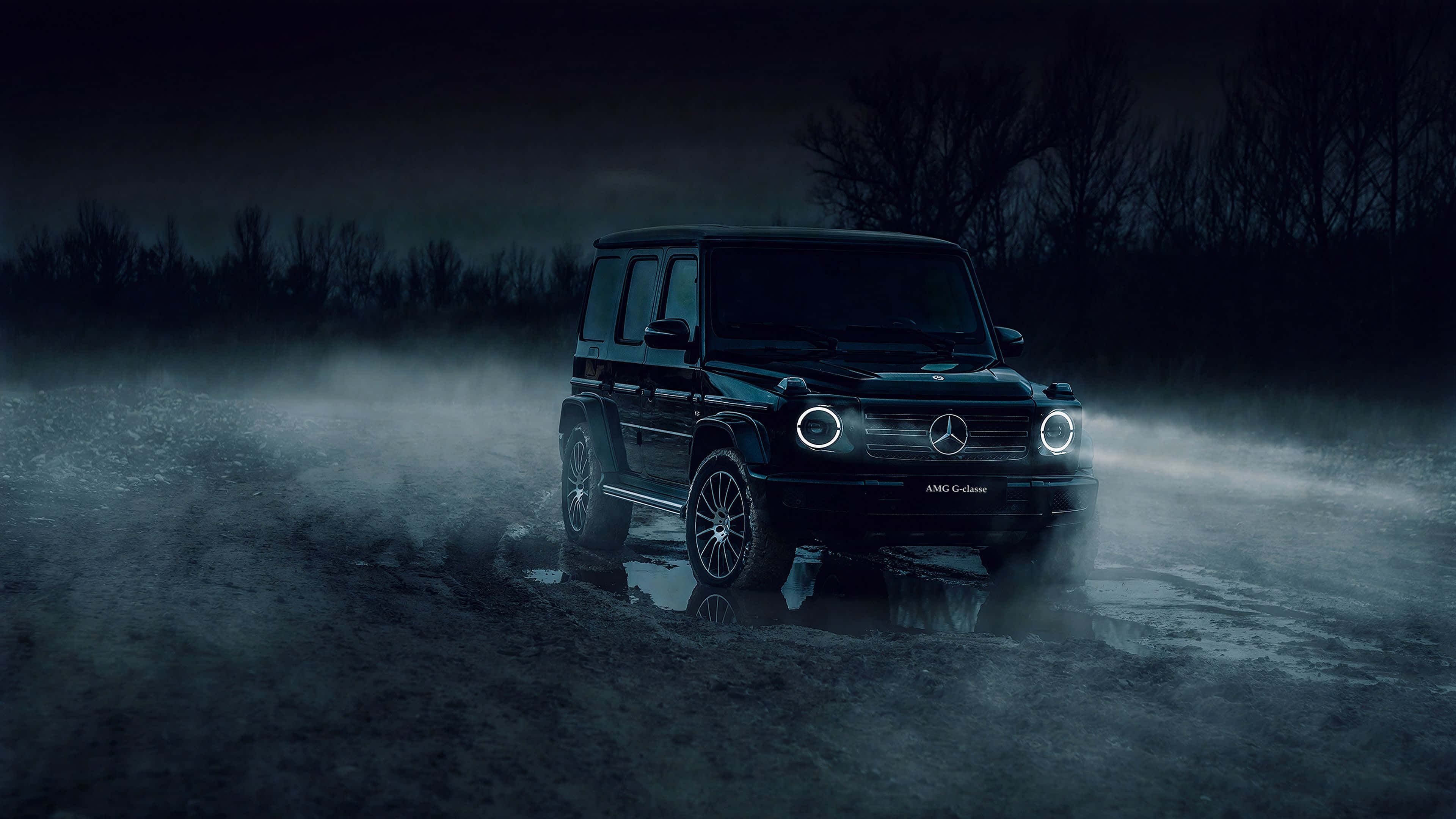 Mercedes 桌布 壁紙 — 一輛黑色梅賽德斯-AMG G-Wagen在黑暗夜空下，穿過霧氣瀰漫的潮濕地形，車頭燈閃閃發光。
