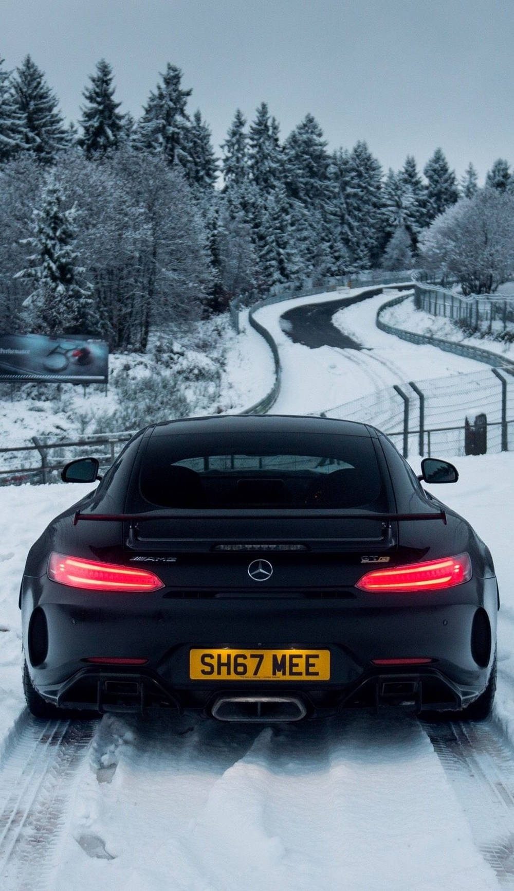 Mercedes 桌布 壁紙 — 一輛黑色梅賽德斯-AMG GT R跑車，紅色尾燈閃爍，在白雪覆蓋的蜿蜒道路上穿過森林行駛。