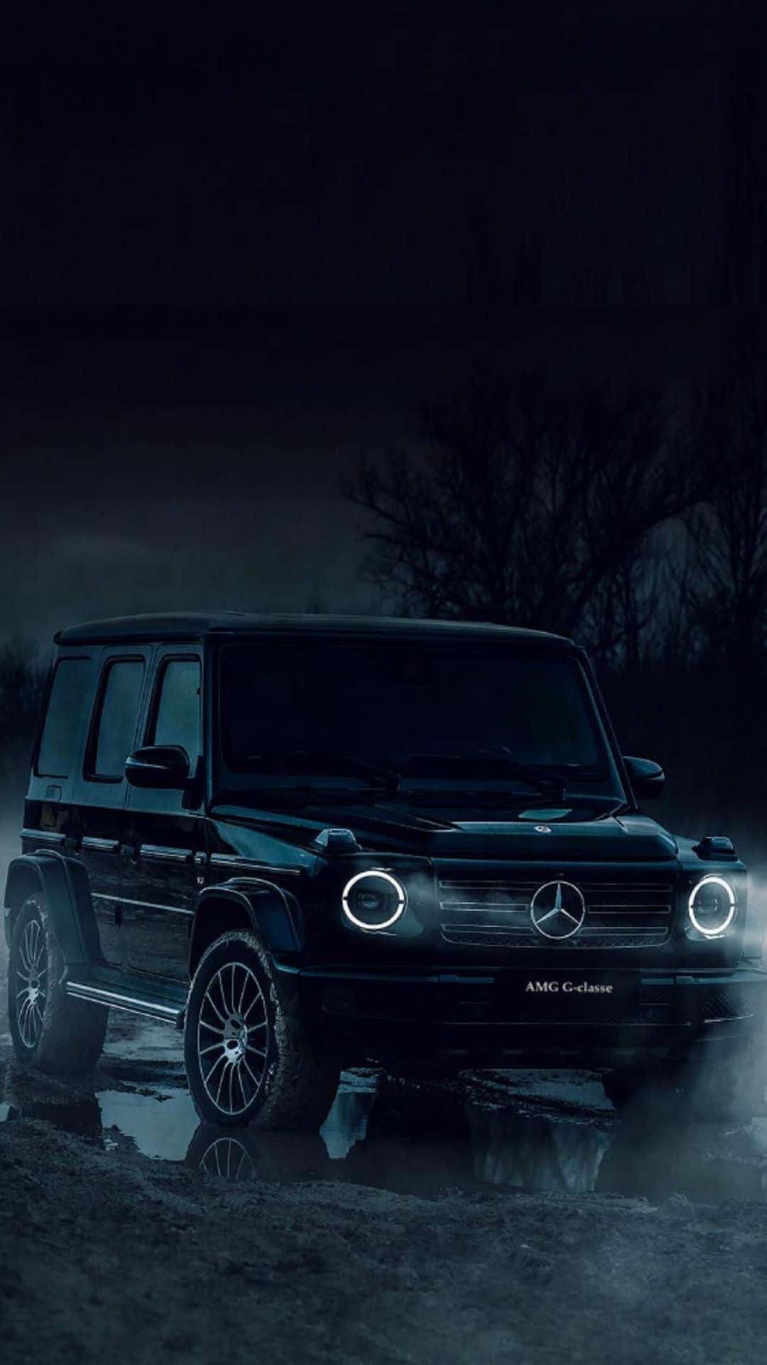 iPhone X Mercedes 桌布 壁紙 — 一輛黑色梅賽德斯-AMG G級SUV，車頭燈發光，夜晚站在霧氣瀰漫的黑暗森林中，倒映在水坑中。