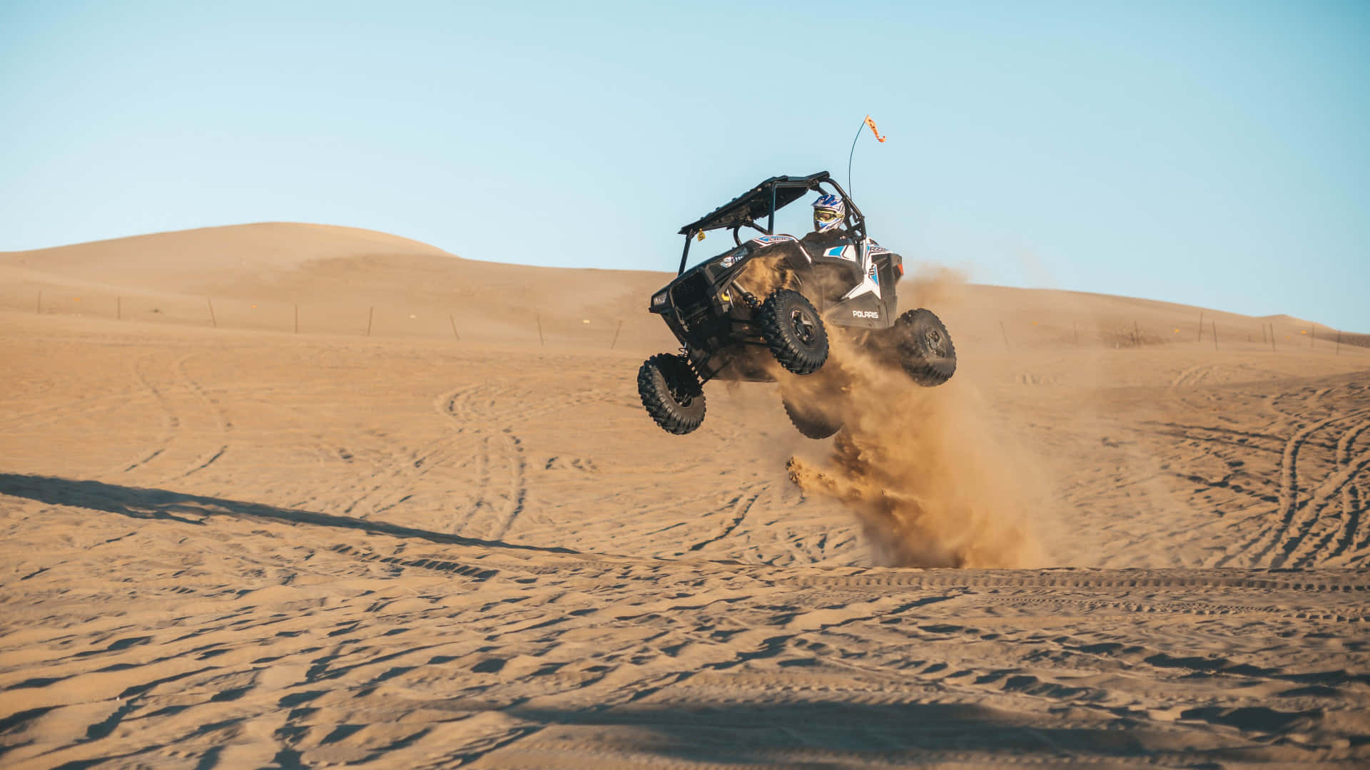 Sand Dunes 桌布 壁紙 — 一輛黑色沙丘越野車在湛藍天空下，飛越金色沙丘，揚起一片塵雲。