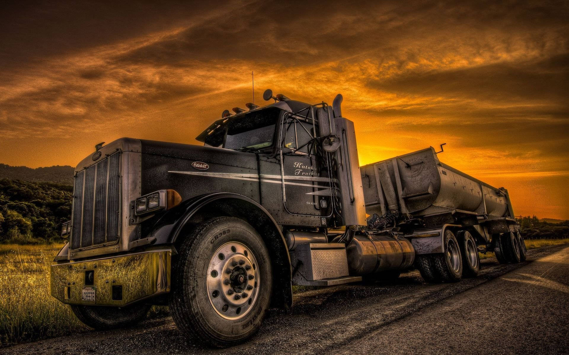 Trucks 桌布 壁紙 — 一輛黑色油罐車停在鄉村道路上，天空呈現火熱的橙色日落和戲劇性的雲彩。