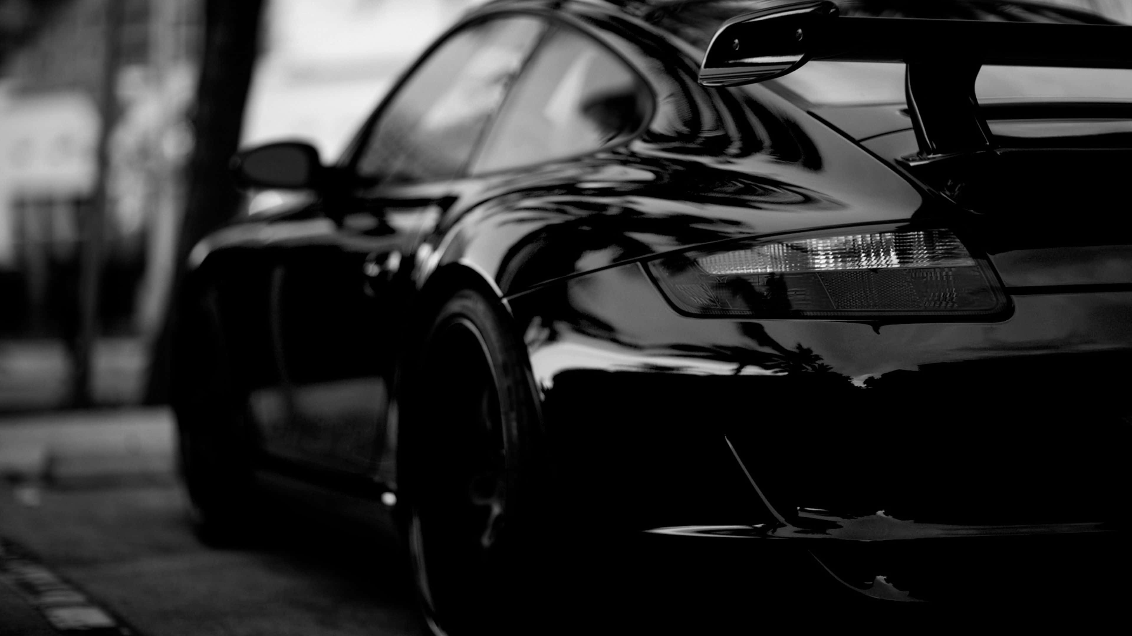 Black Car 4K 桌布 壁紙 — 一輛黑色流線型跑車配備後擾流板，單色調停放在城市街道上。