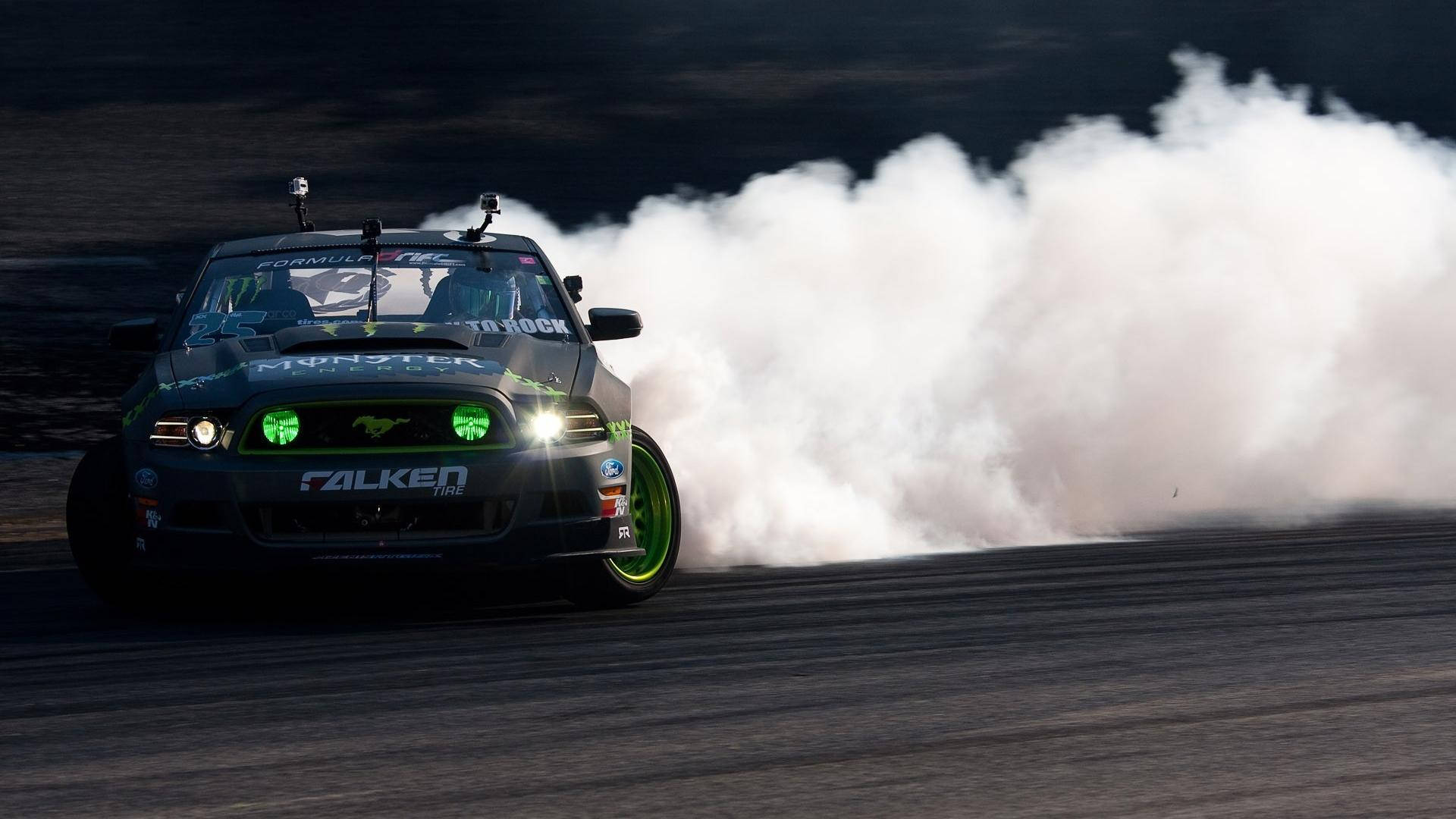 Auto Racing 桌布 壁紙 — 一輛黑色漂移車帶有發光的綠色頭燈，在黑暗的賽道上側滑時冒出濃煙。