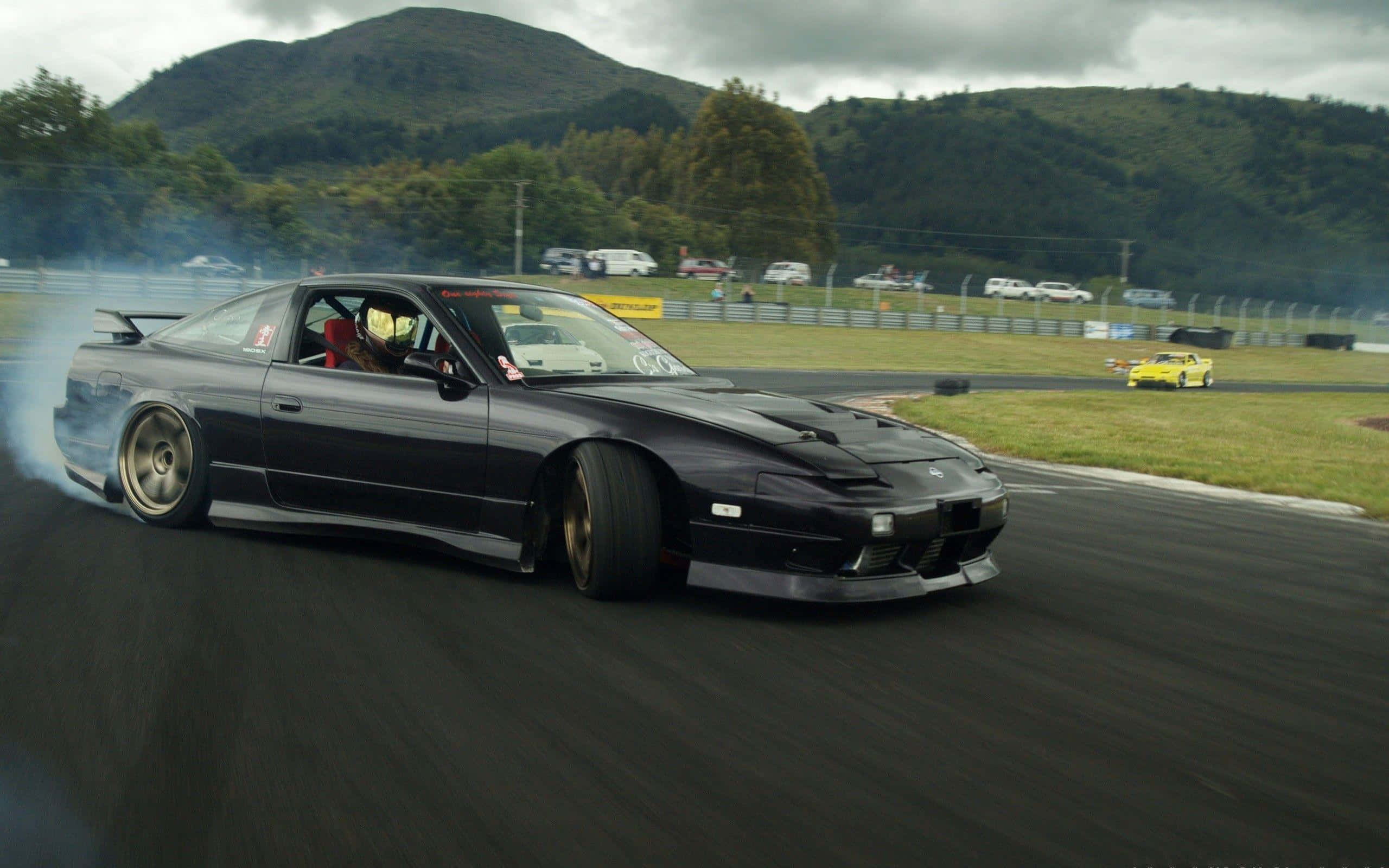 Nissan 180sx 桌布 壁紙 — 一輛黑色甩尾車在潮濕的賽道上冒煙，背景有山脈和樹木。