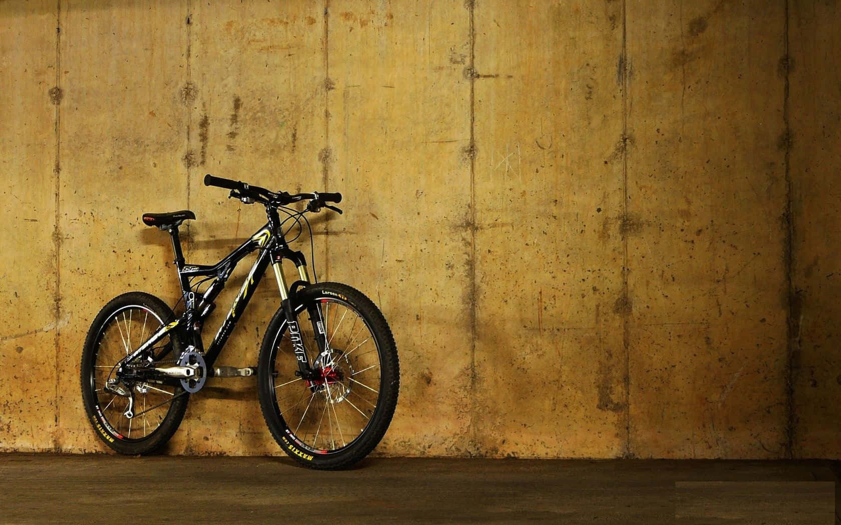 Mtb 桌布 壁紙 — 一輛黑色登山自行車靠在一間光線昏暗的室內空間的紋理黃色混凝土牆上。