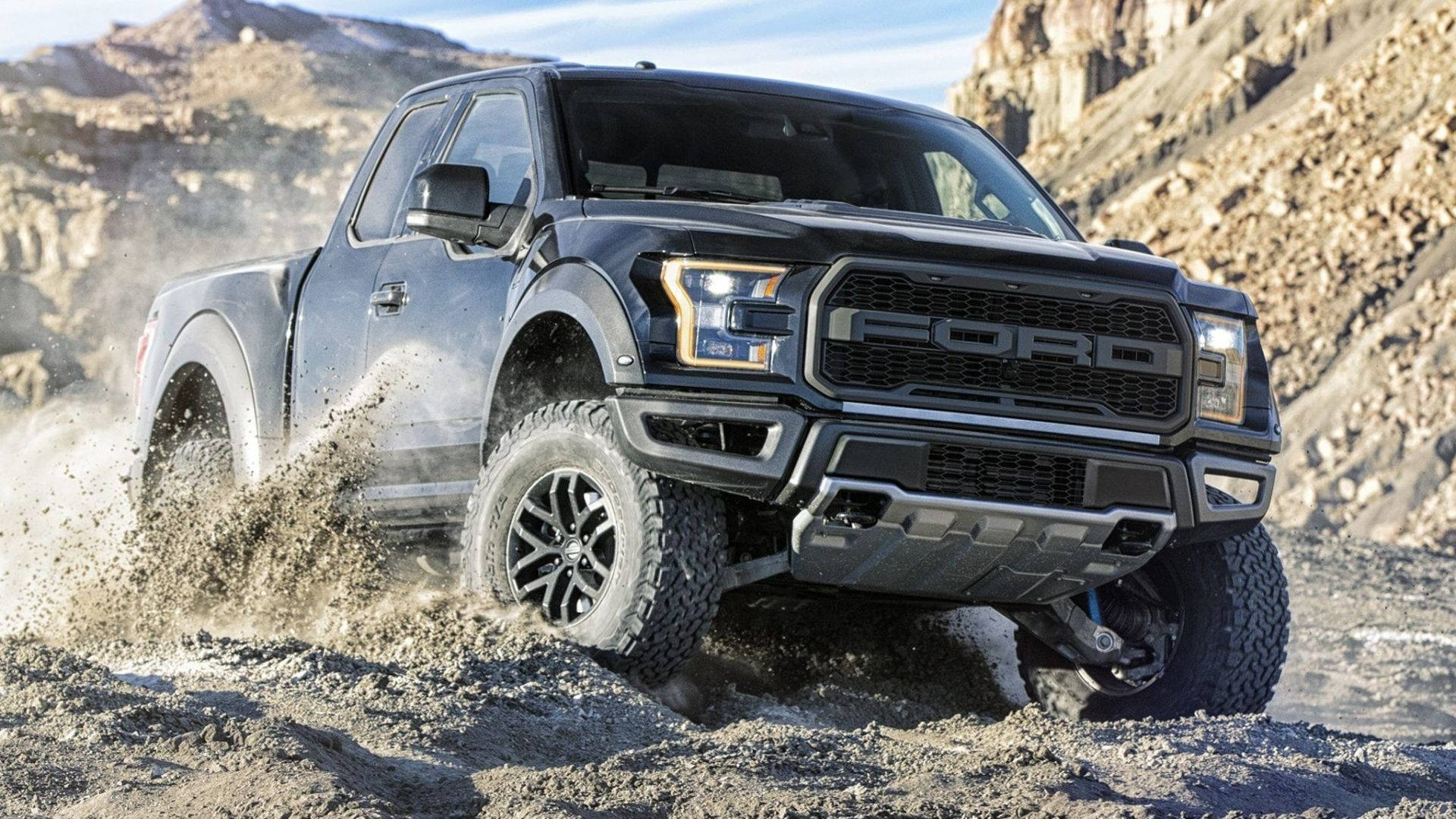 Raptor 桌布 壁紙 — 一輛黑色福特 F-150 Raptor 卡車在明亮的日光下，在崎嶇的泥濘地形上行駛，揚起泥漿和灰塵。
