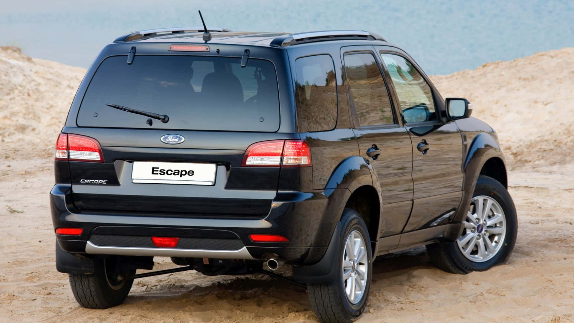 Ford Escape 桌布 壁紙 — 一輛黑色福特Escape SUV停放在沙地上，背景是海洋。
