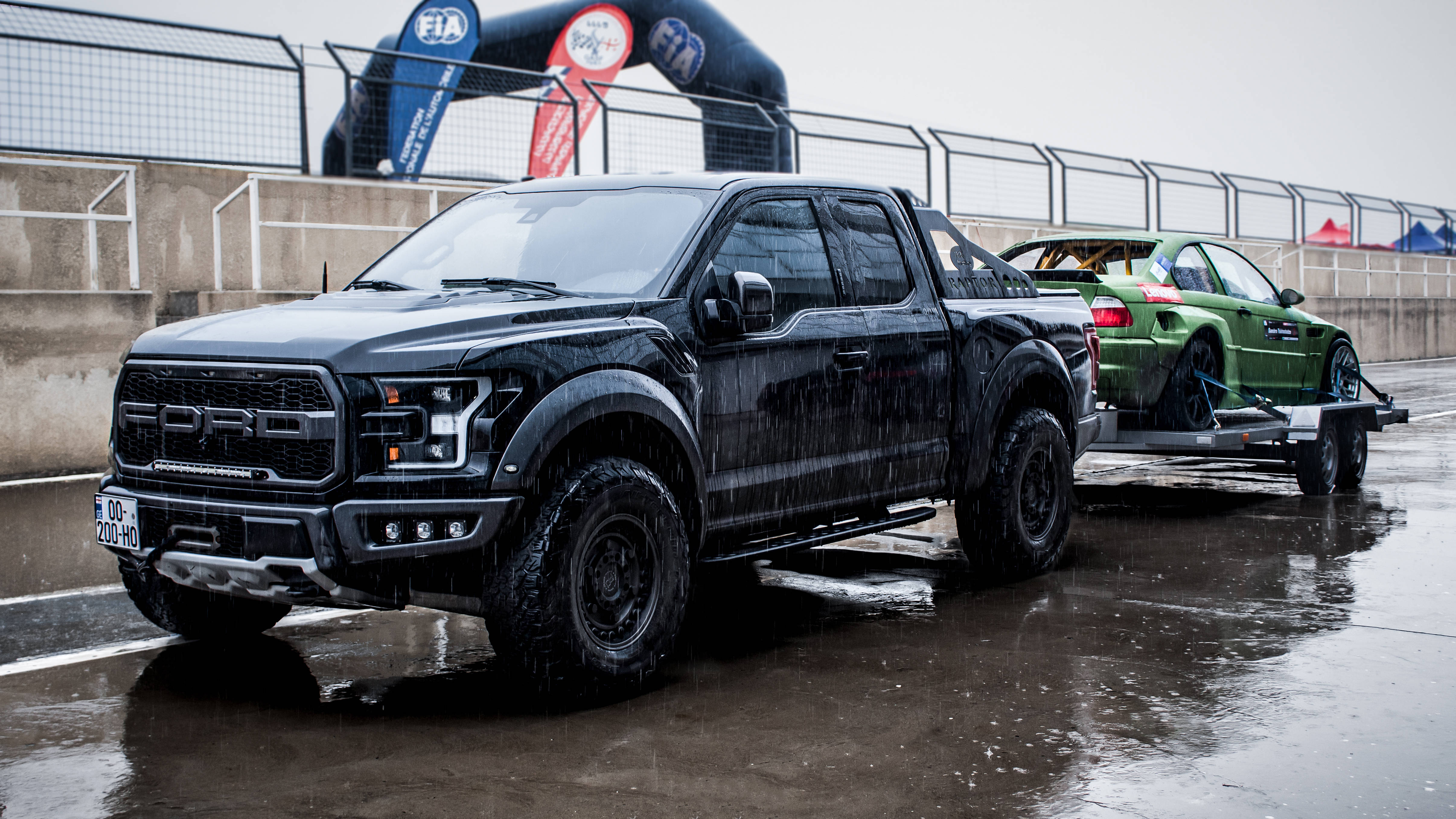 Racing 桌布 壁紙 — 一輛黑色福特F-150猛禽皮卡在陰天下拖著一輛綠色賽車在潮濕的賽道上。
