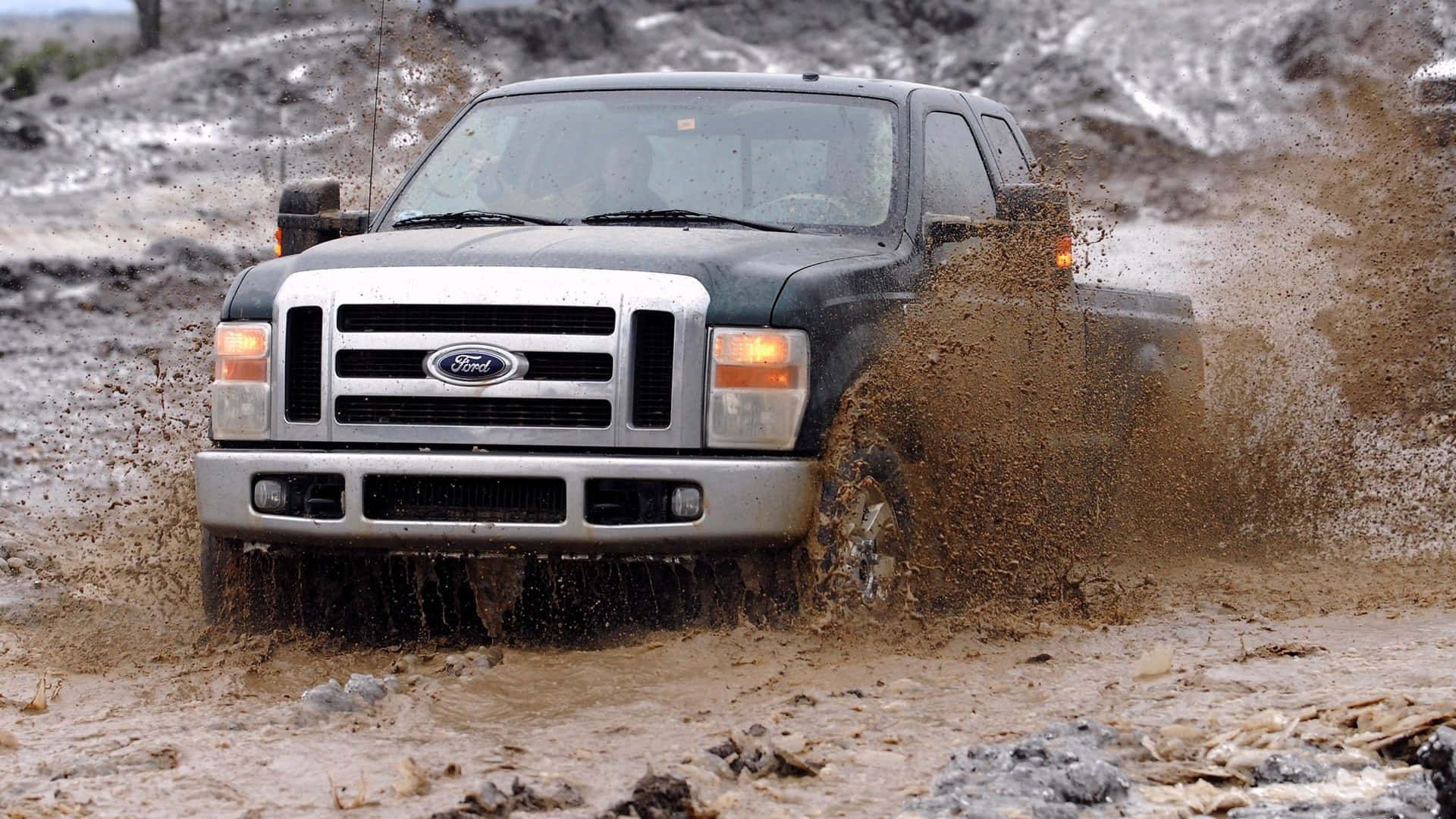 Ford Truck 桌布 壁紙 — 一輛黑色福特卡車在厚厚的棕色泥漿中行駛，穿過泥濘地形時濺起水滴。